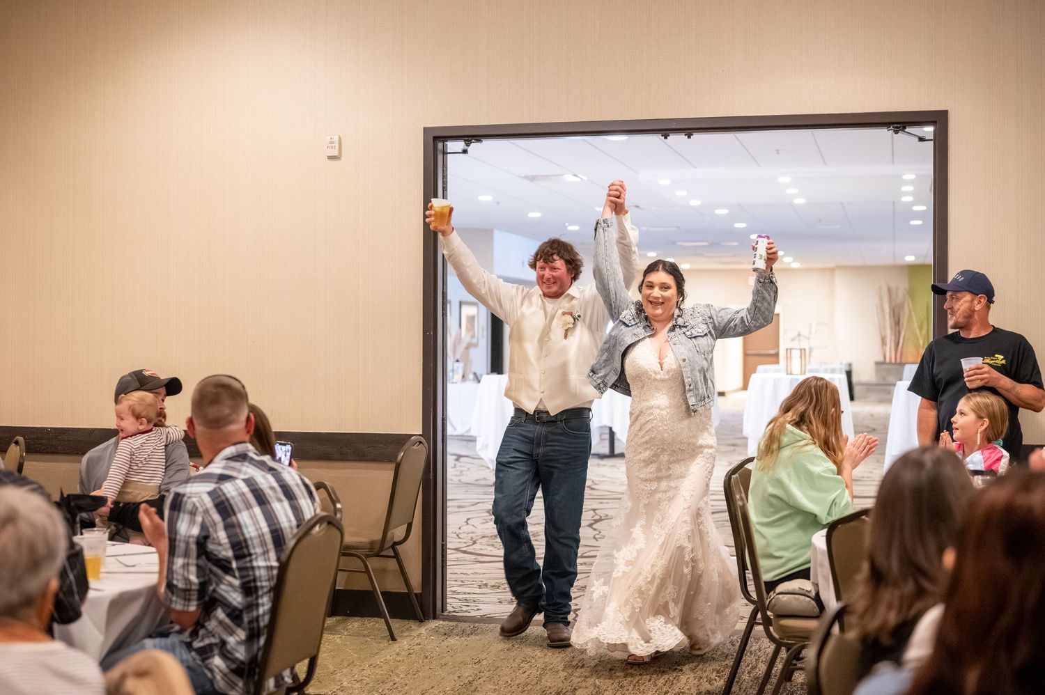 Wedding couple making their grand entrance into a reception hall filled with seated guests.