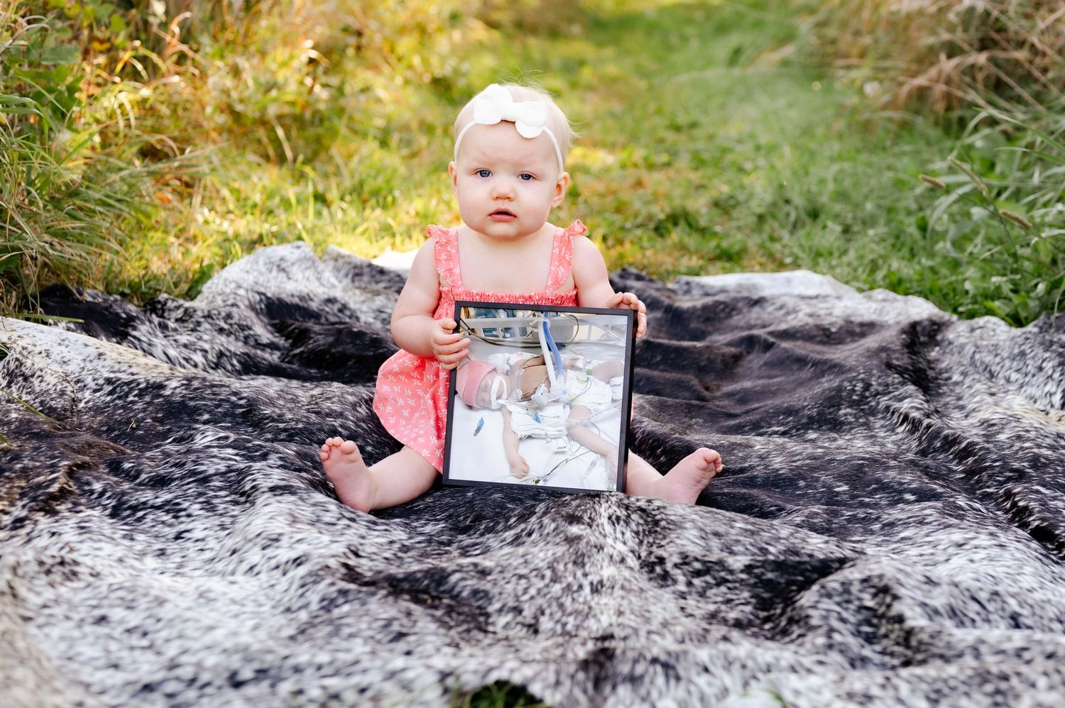 A toddler in a coral dress sits on a gray blanket holding a framed photo.
