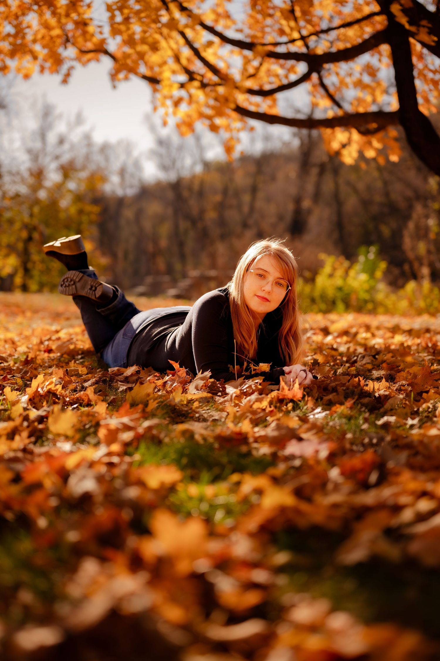 A person lies on autumn leaves under orange foliage in a park during golden hour.