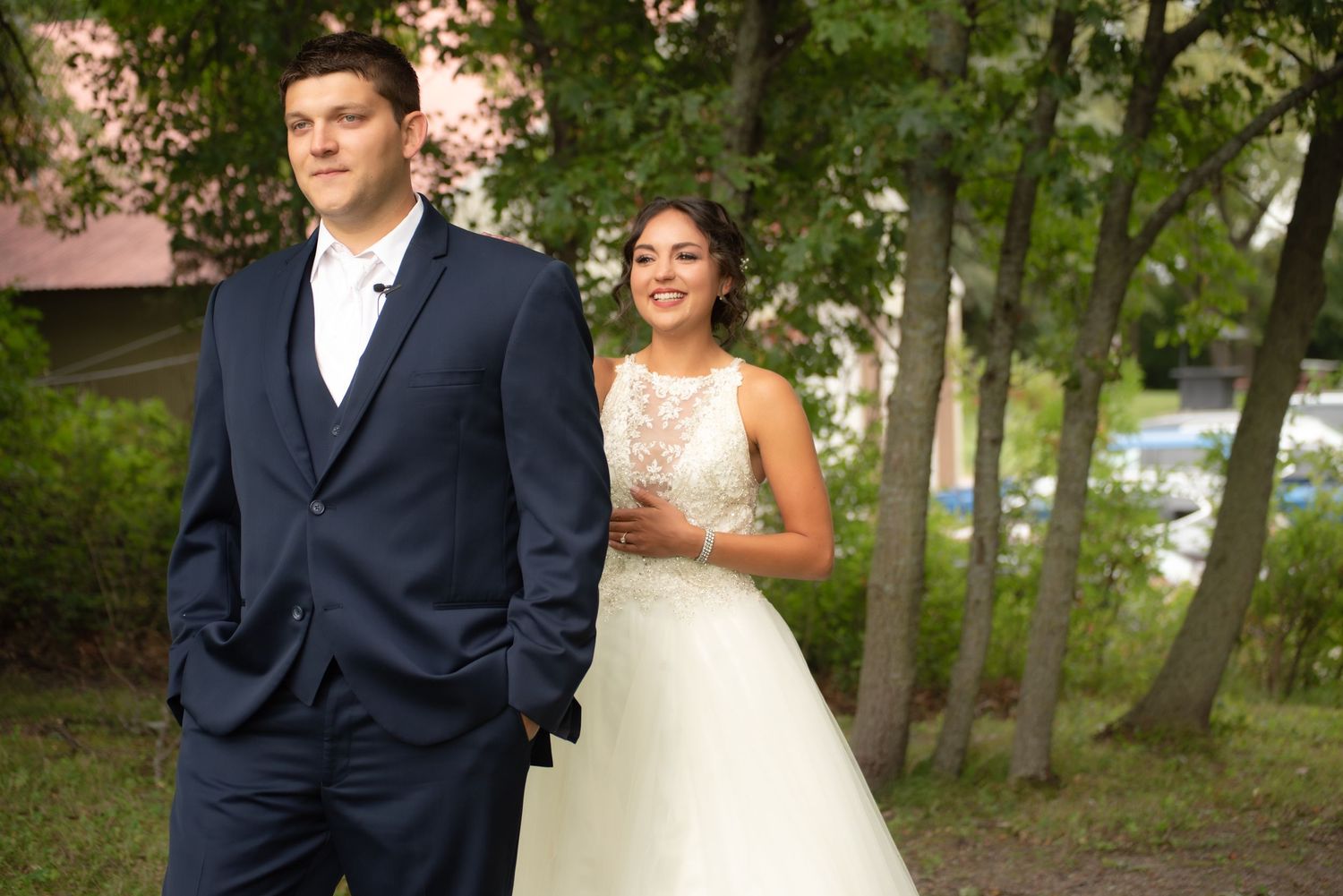 Stylish wedding portrait in forest setting with groom in foreground and bride behind.