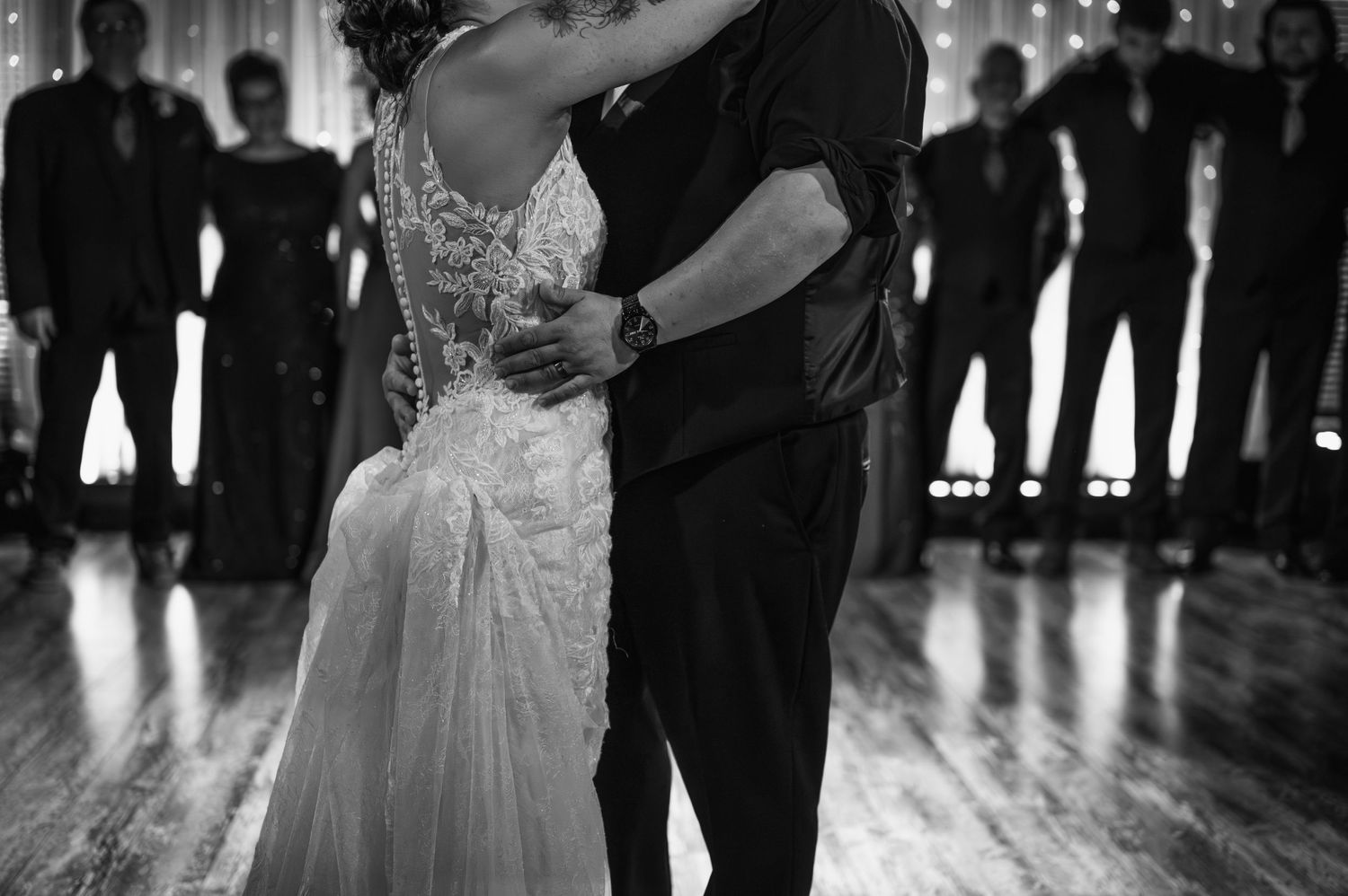 Black and white photo of newlyweds dancing with silhouettes of guests in the background.