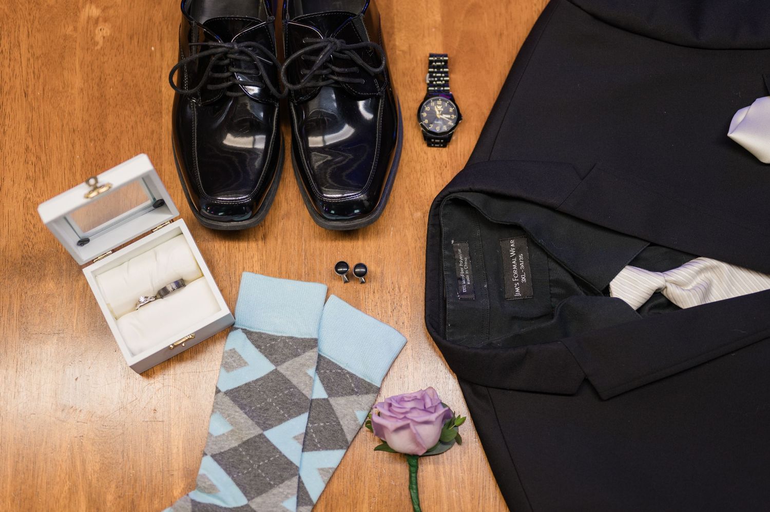 Groom's wedding accessories including patent shoes, socks, watch and boutonniere laid flat.