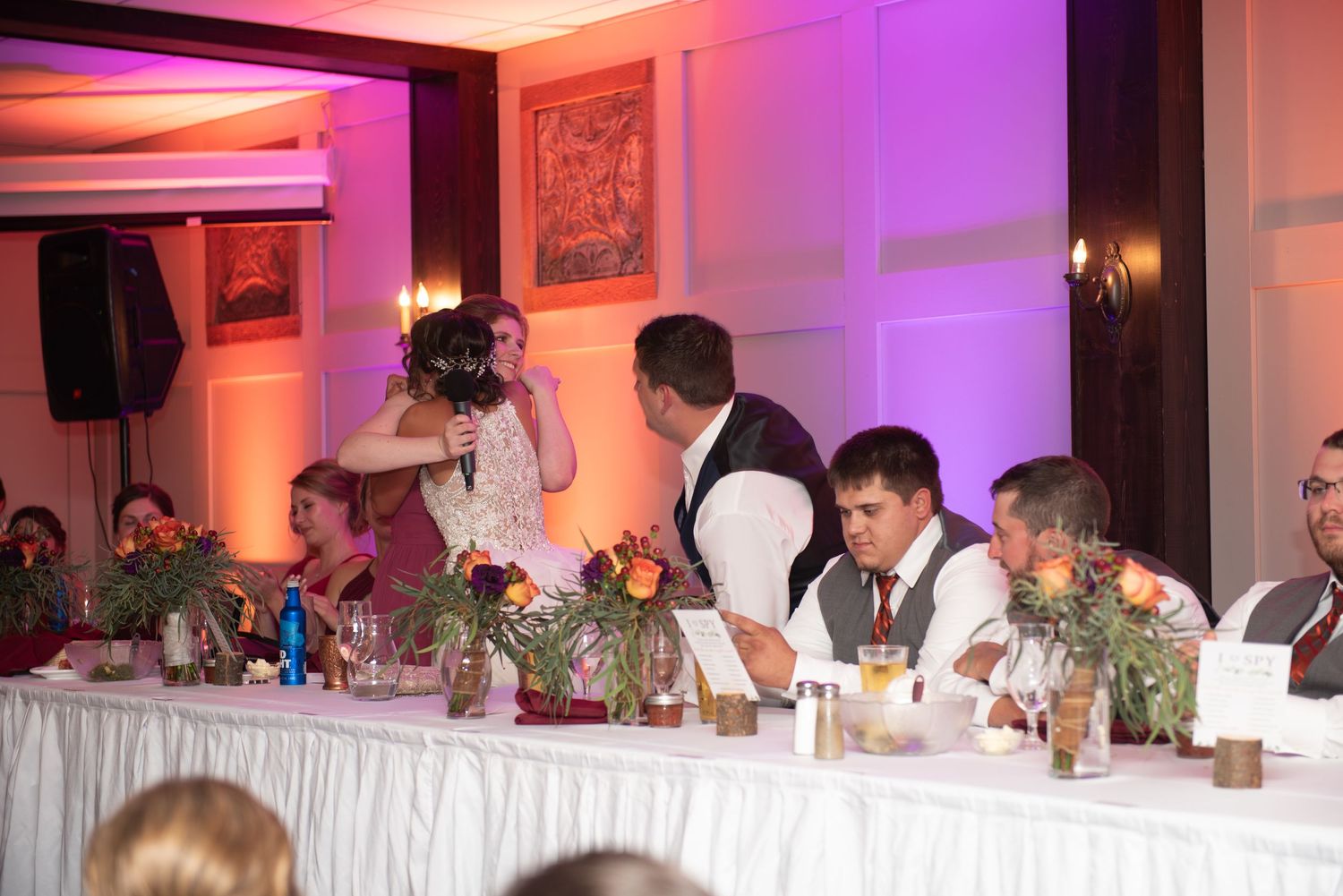 Wedding reception head table with purple uplighting and floral centerpieces at an elegant venue.