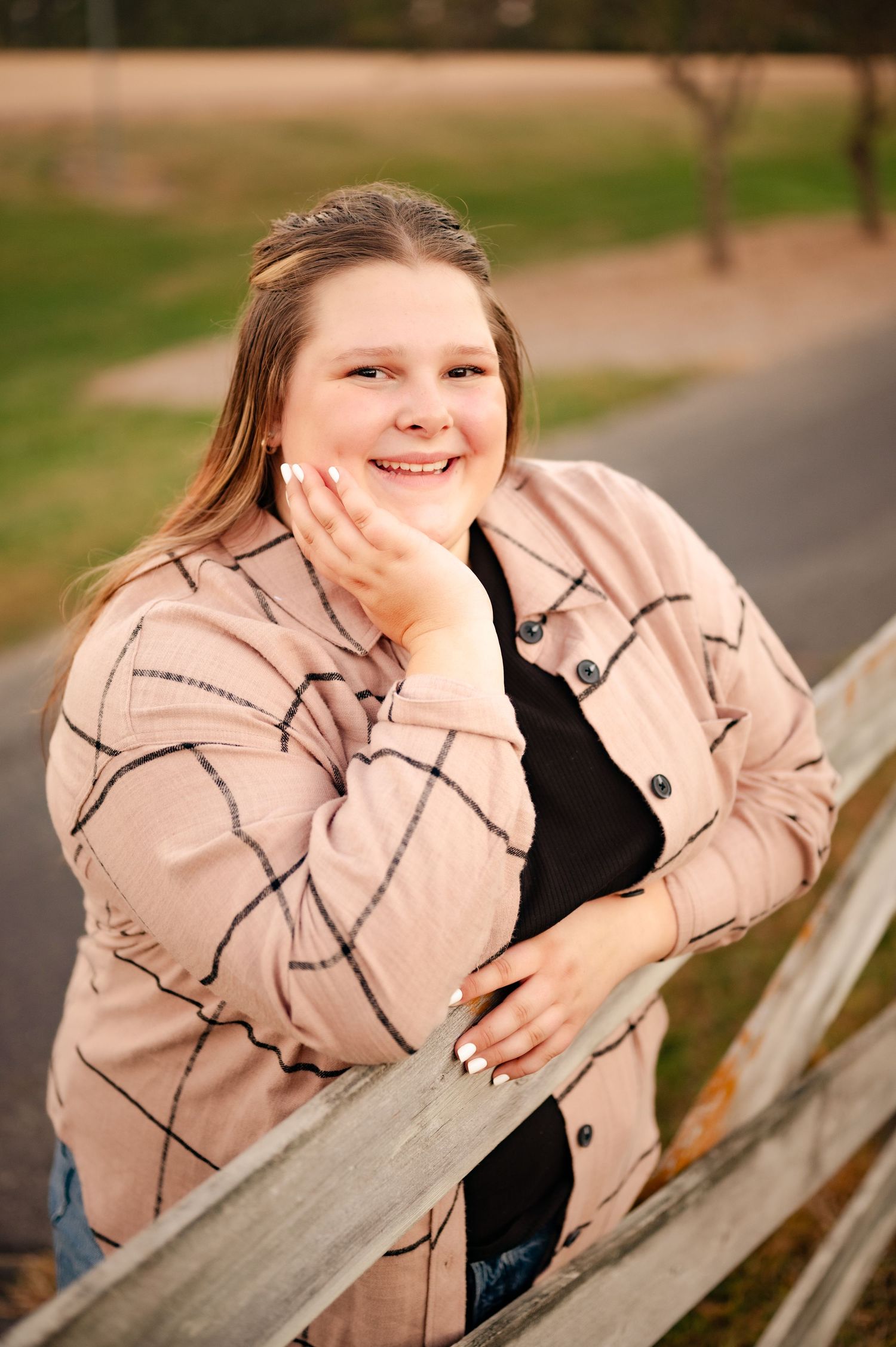 Person posing by wooden fence wearing beige patterned jacket during sunset.