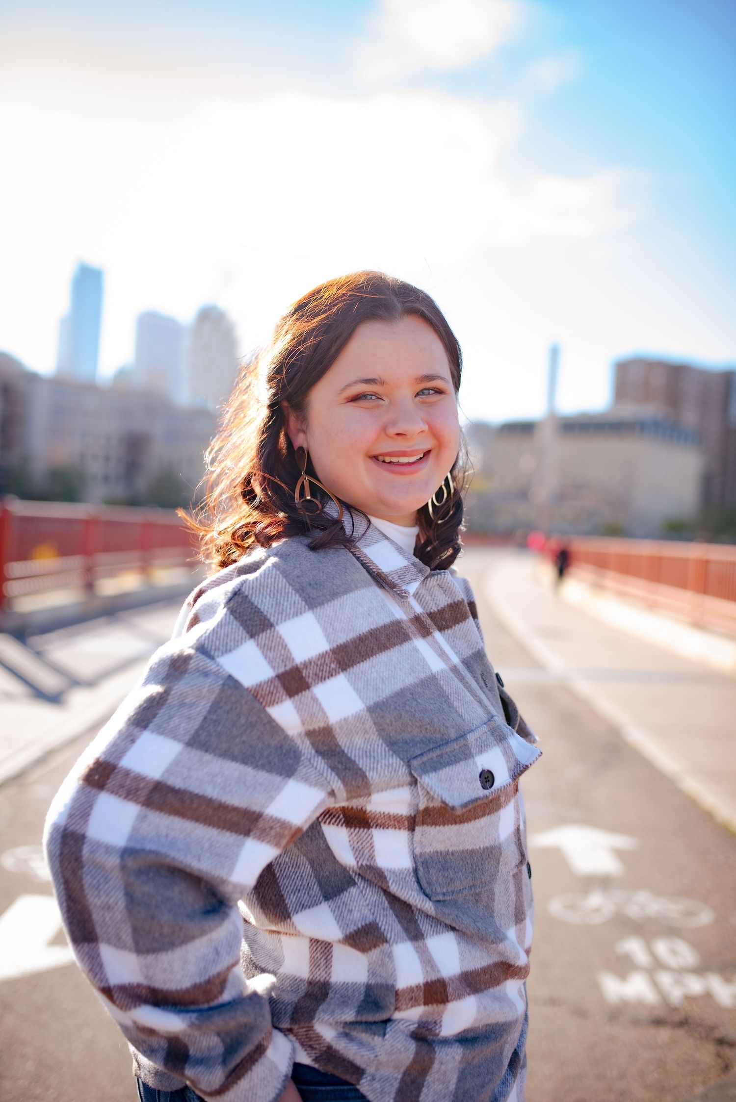 Person in plaid flannel smiling with city skyline in background on sunny day.