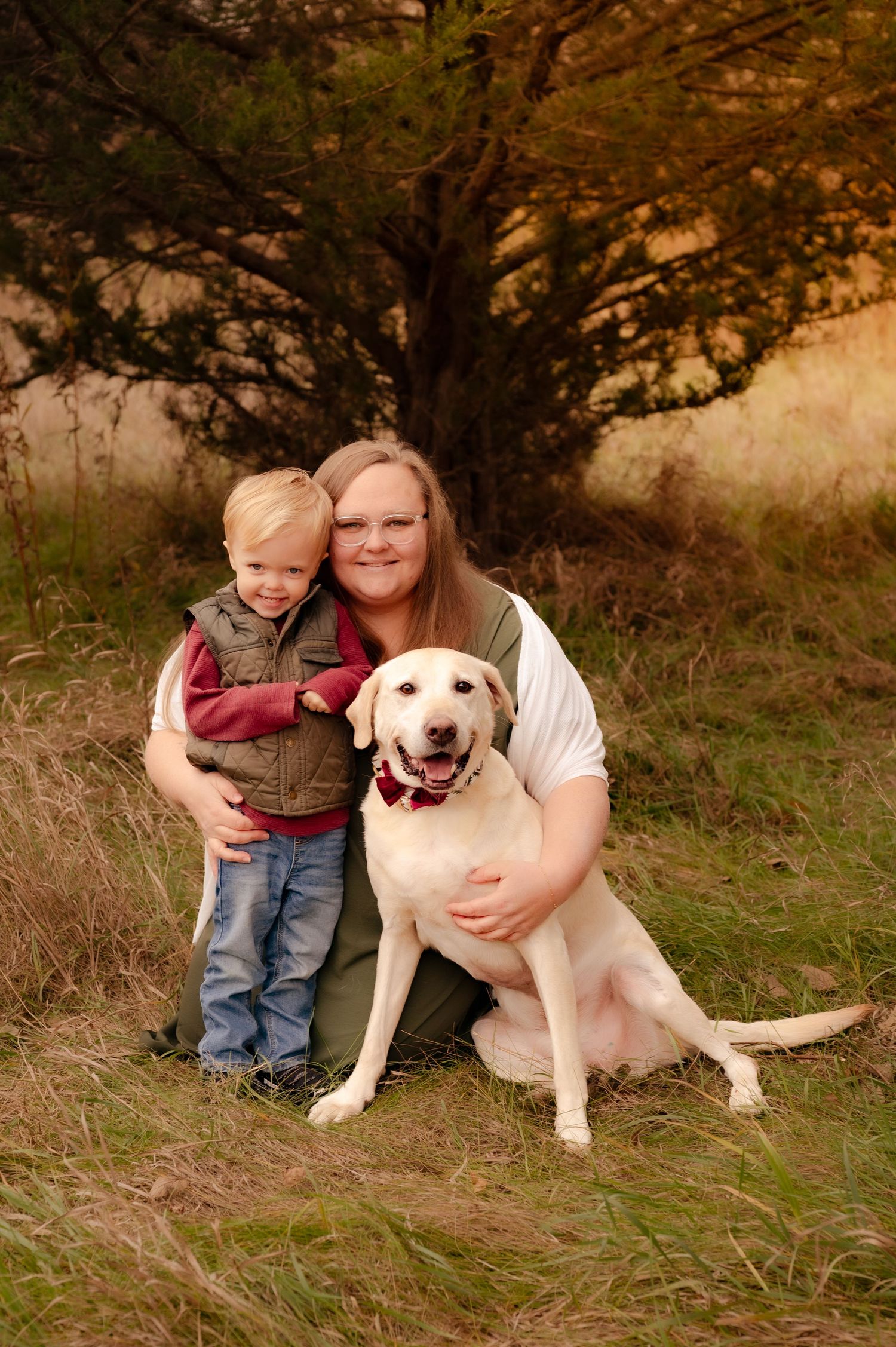A heartwarming outdoor scene with a young child and adult sitting alongside a friendly white Labrador dog.