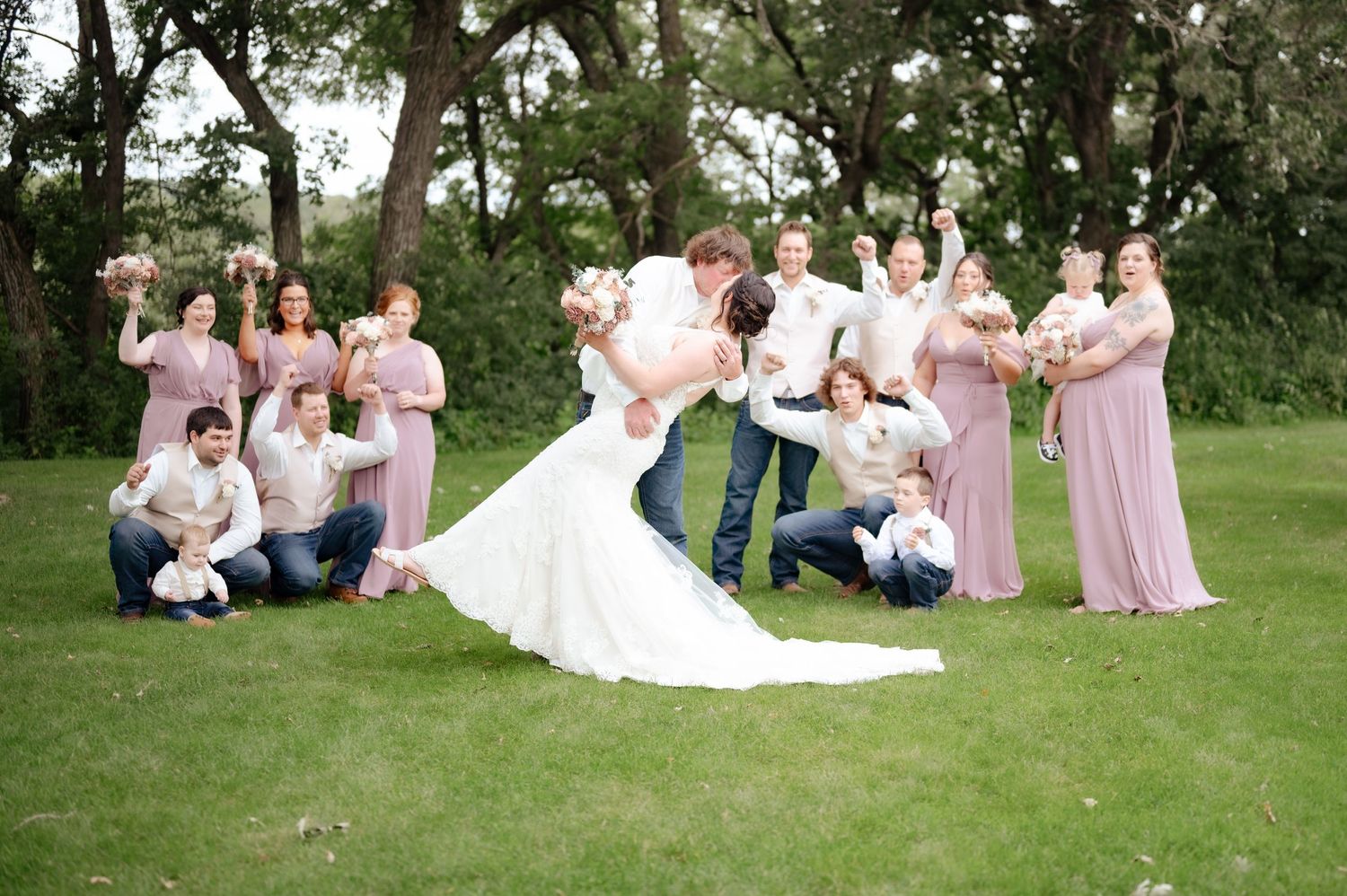 Wedding party in mauve dresses celebrating on a green lawn during an outdoor ceremony.