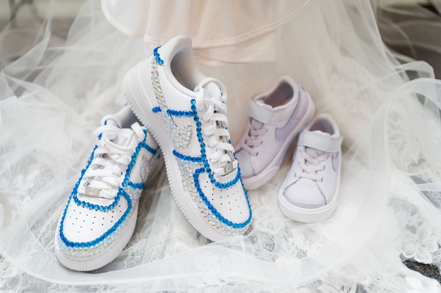 Three pairs of wedding sneakers in white and blue displayed on tulle fabric.