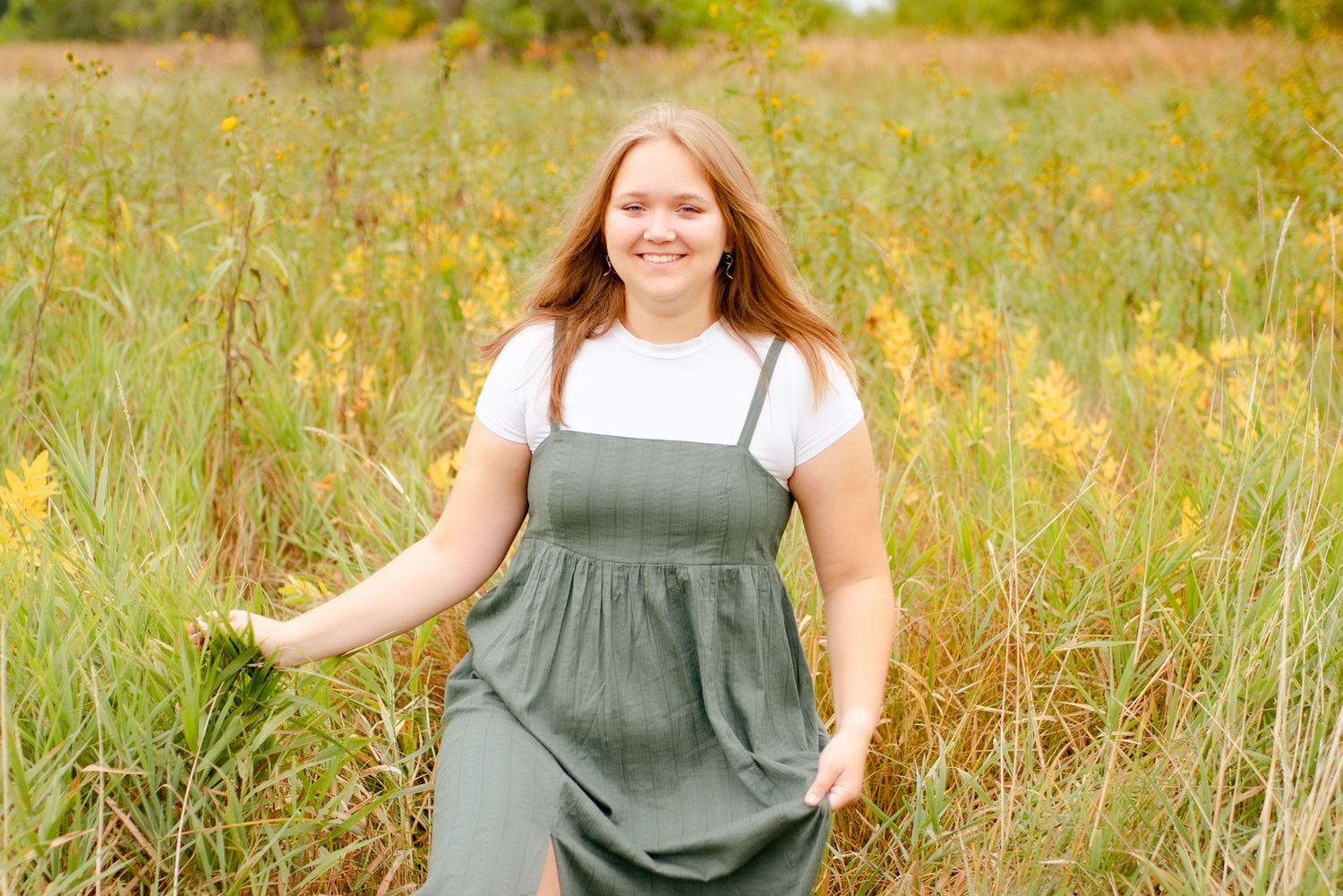 Person wearing olive green overalls twirling in a summer meadow.