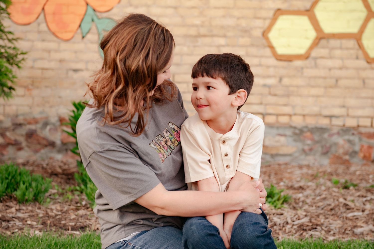 Candid moment of affectionate interaction against a brick wall with colorful honeycomb and flower mural artwork.