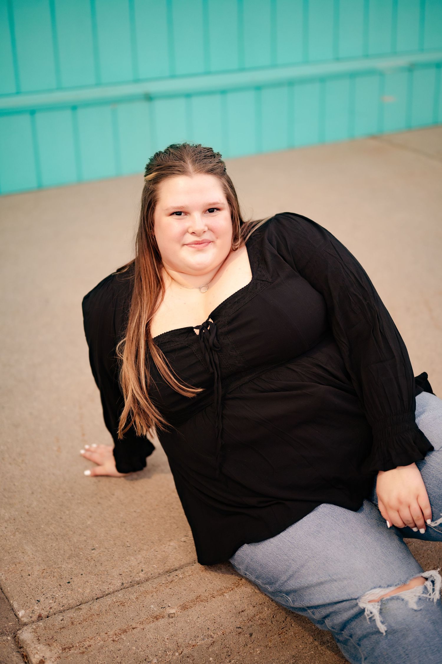 Person in black outfit sitting against turquoise wall background.
