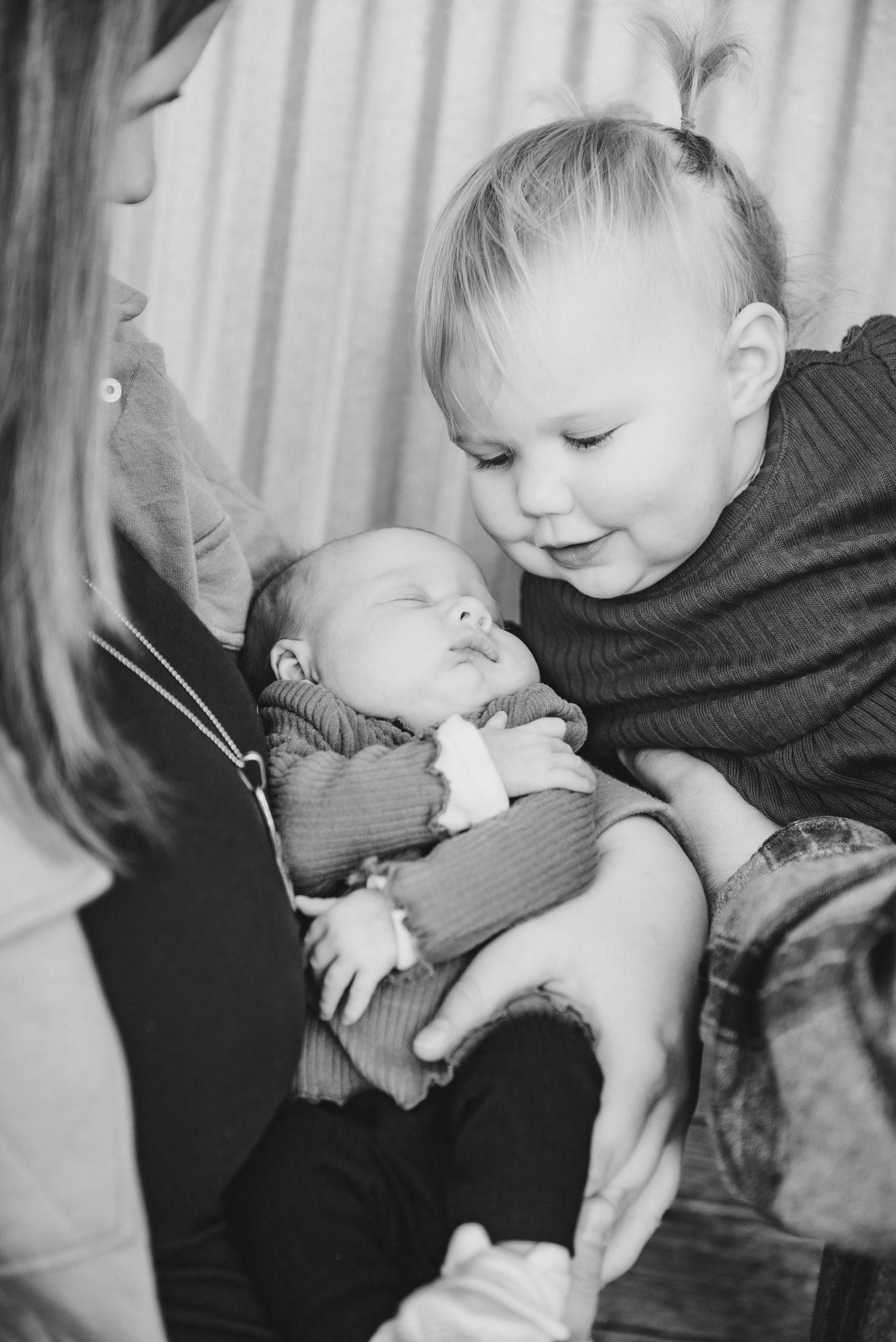 Black and white photo of siblings bonding with newborn baby.