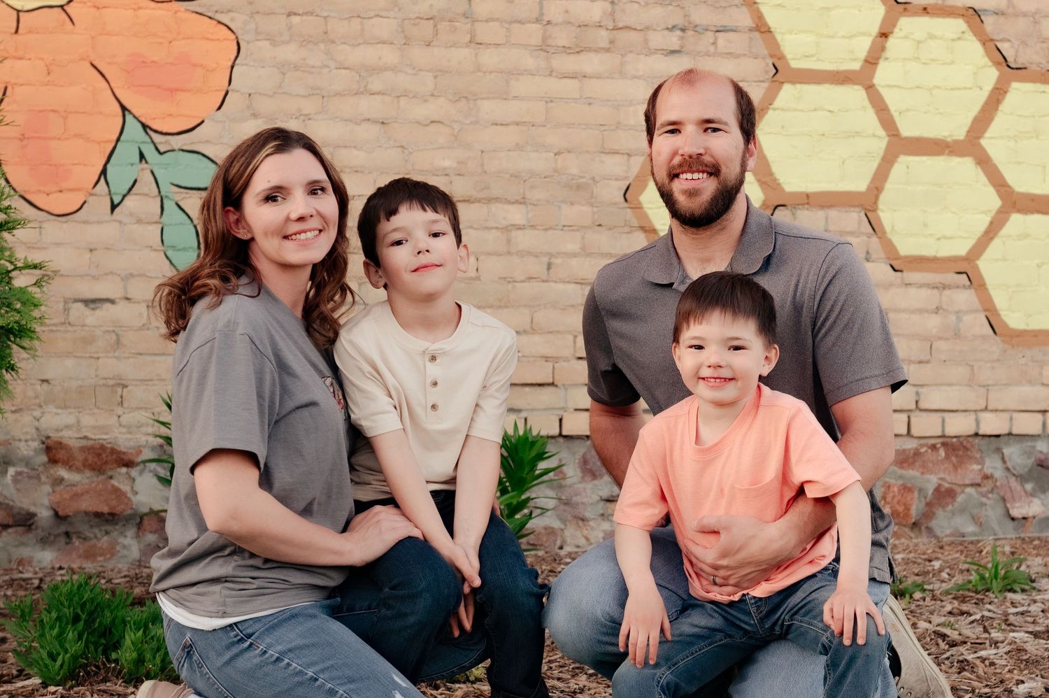 Family of four sits together against a brick wall decorated with honeycomb patterns.