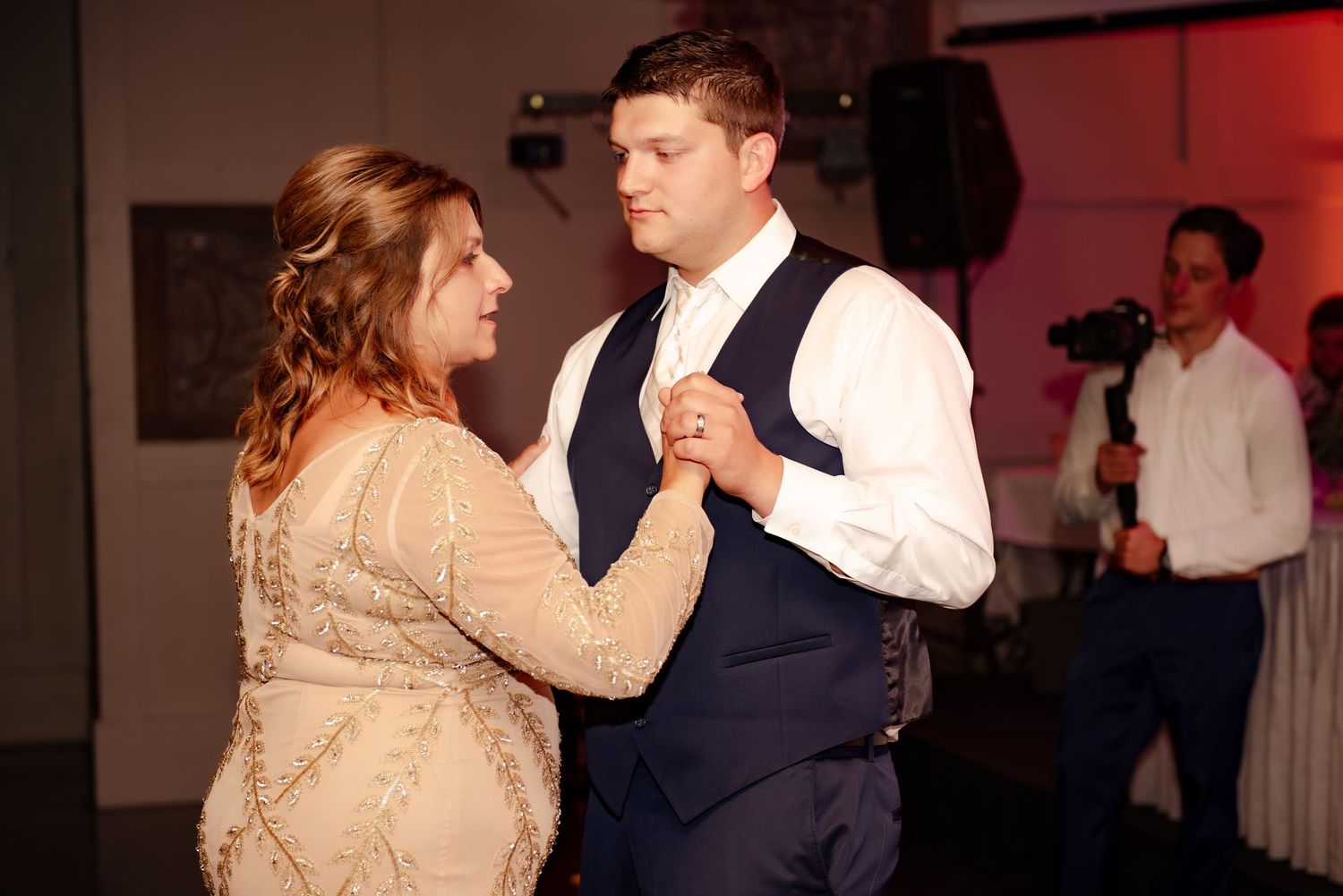 Couple dancing together at wedding reception with guests in background.