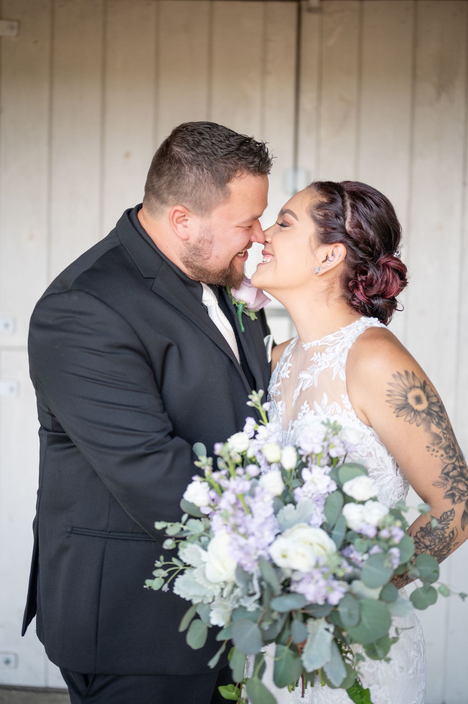 Close-up of newlyweds sharing romantic moment with purple and white bouquet.