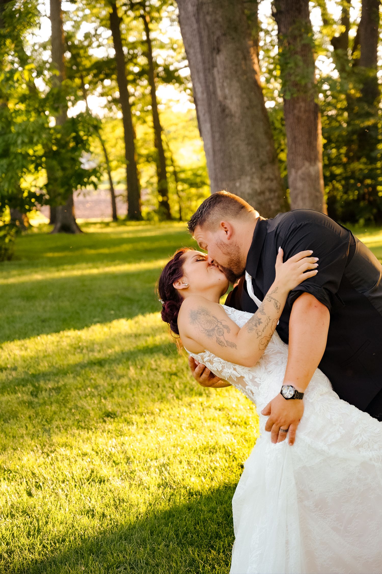 Intimate dip kiss between newlyweds in golden evening sunlight amongst trees.