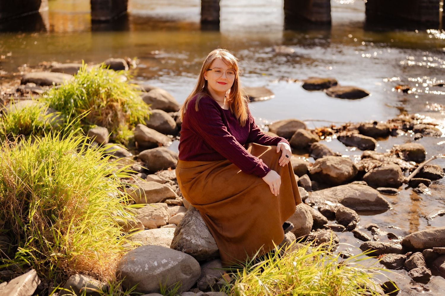 Outdoor portrait by river with rocks and ornamental grasses in golden sunlight.