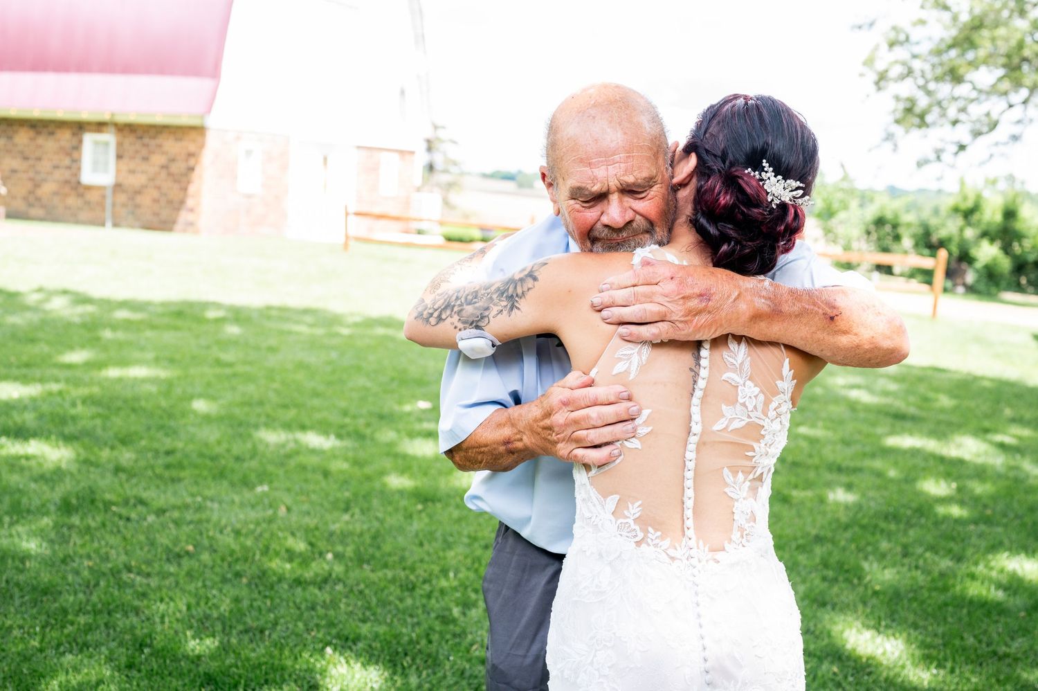 Emotional embrace at outdoor wedding with white lace dress and rustic barn backdrop.