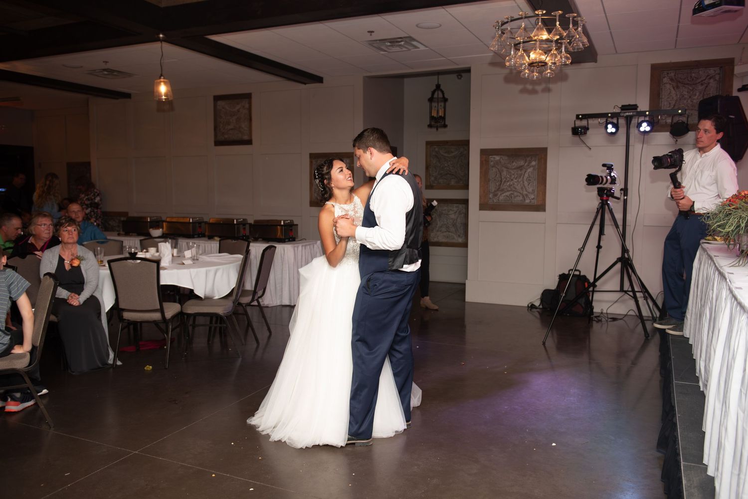 A couple shares their first dance at a wedding reception in a venue with elegant lighting and decor.