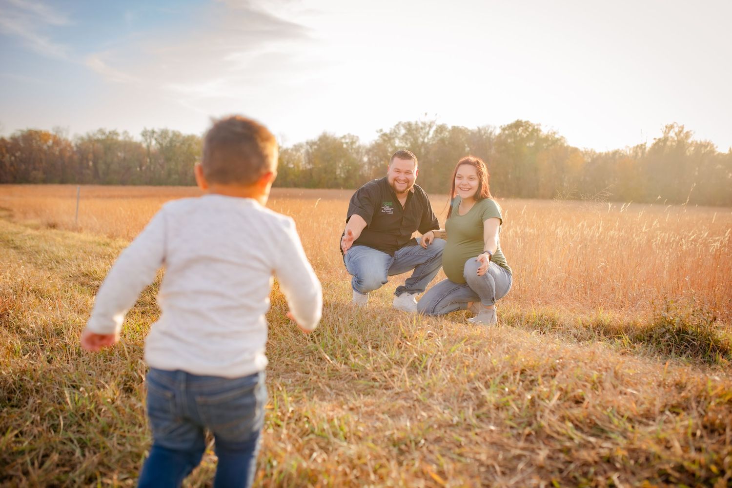 Child running towards family members in a sunlit autumn field.
