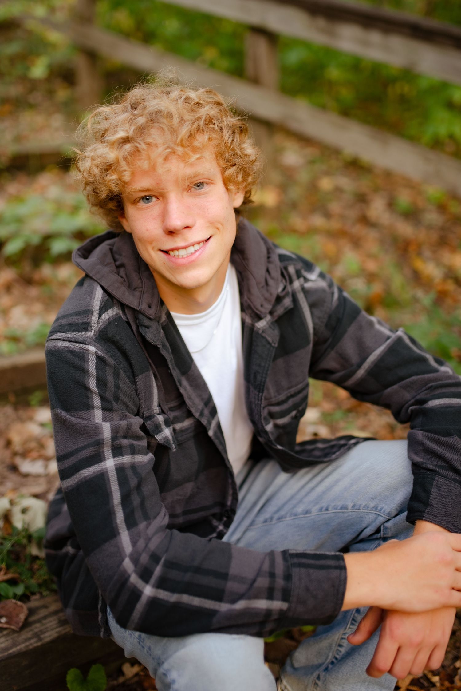 Outdoor portrait of someone sitting casually on wooden steps wearing a plaid jacket and jeans in autumn.