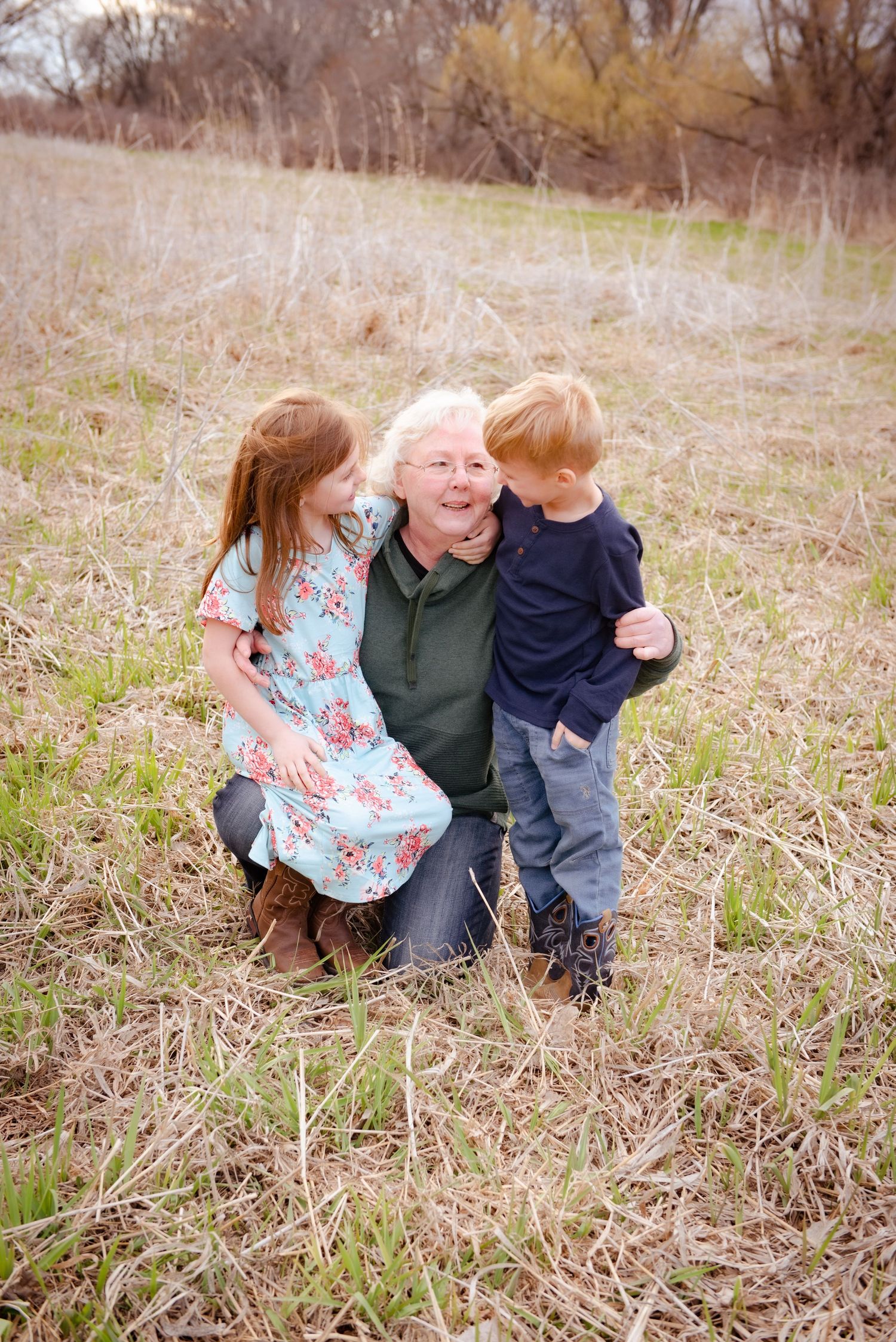 Three people sharing joyful embraces and smiles while kneeling in tall grass.