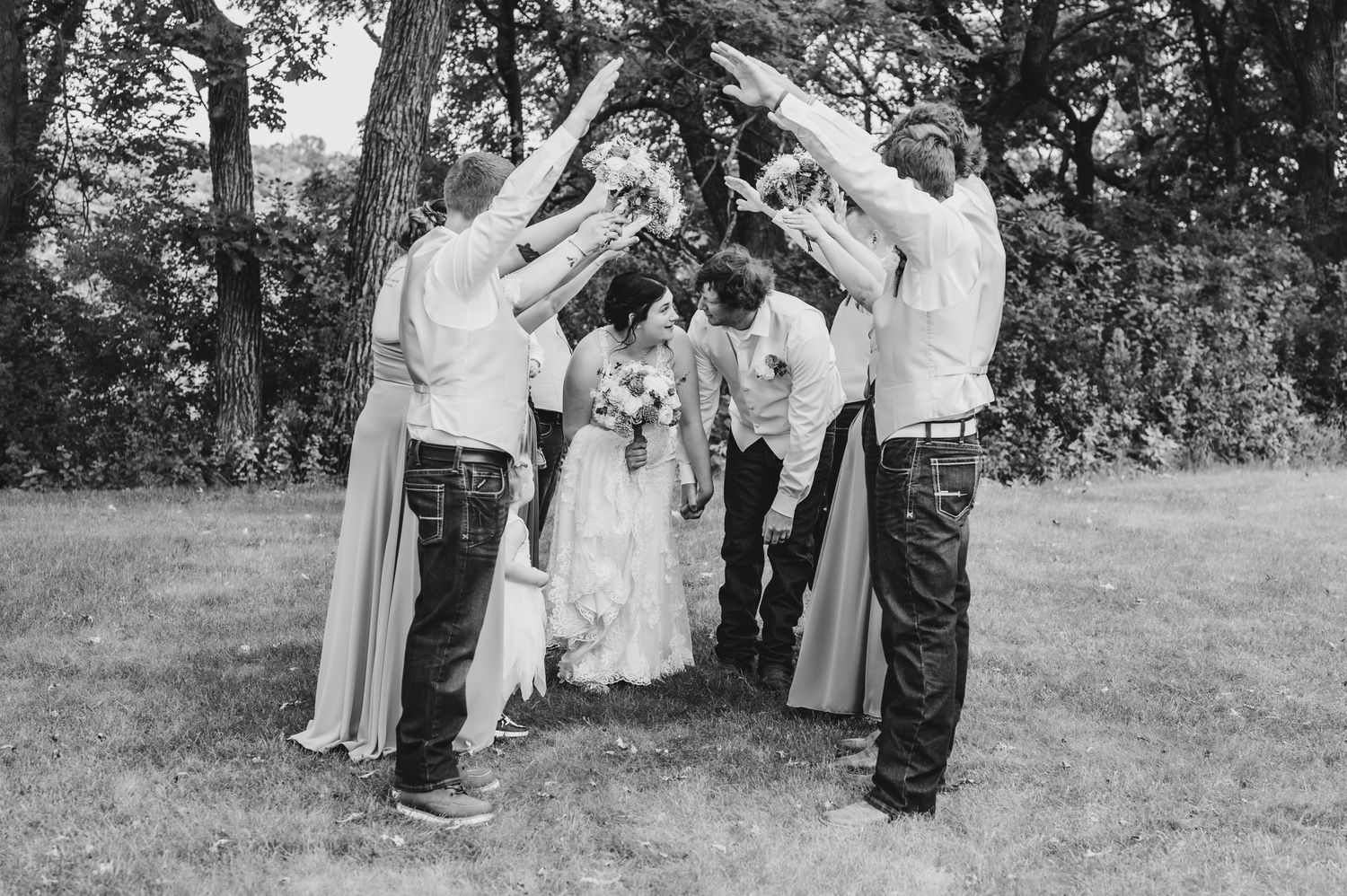 Wedding party forms celebratory arch tunnel for couple in black and white photo.