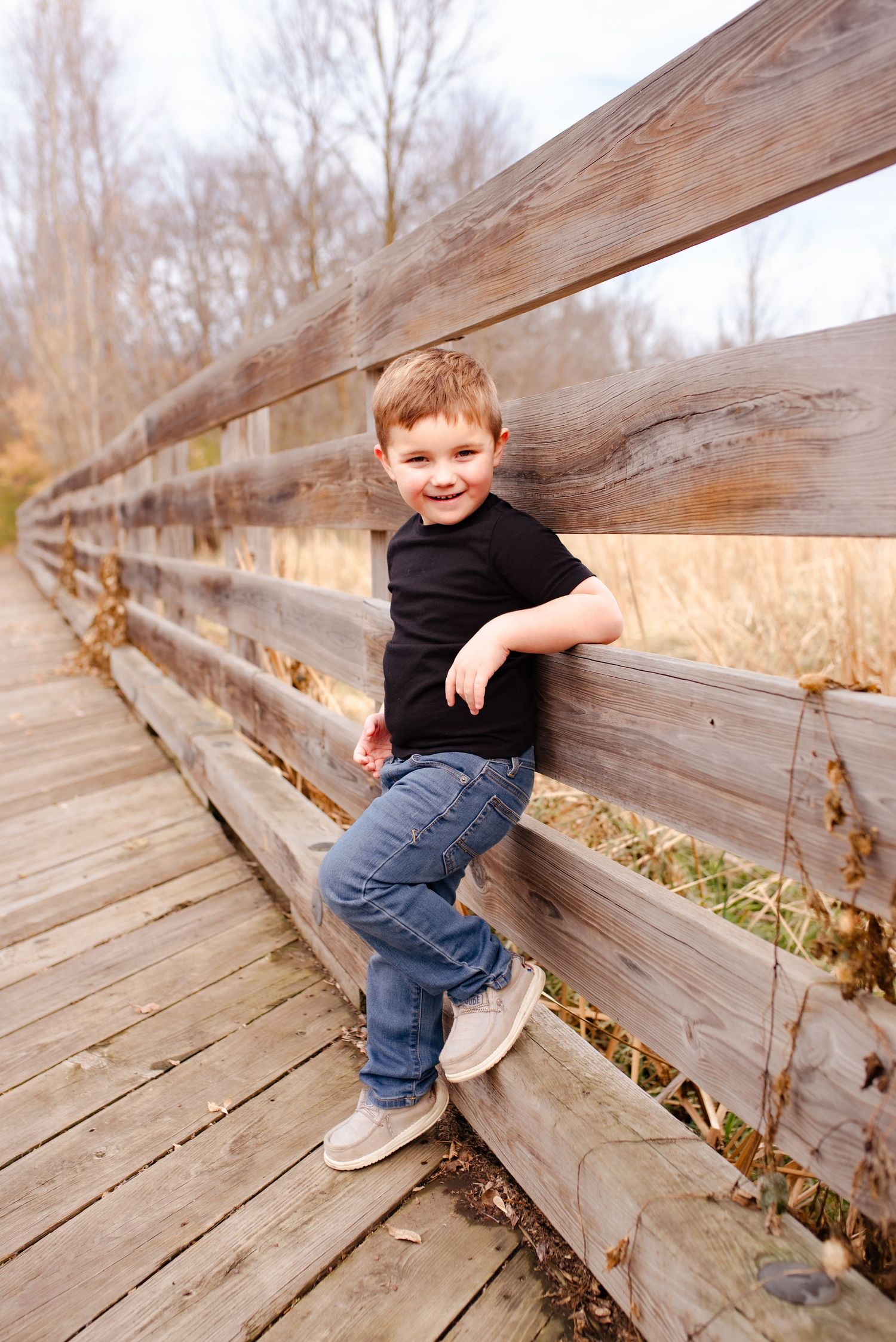 Young child in black shirt poses on wooden bridge railing.