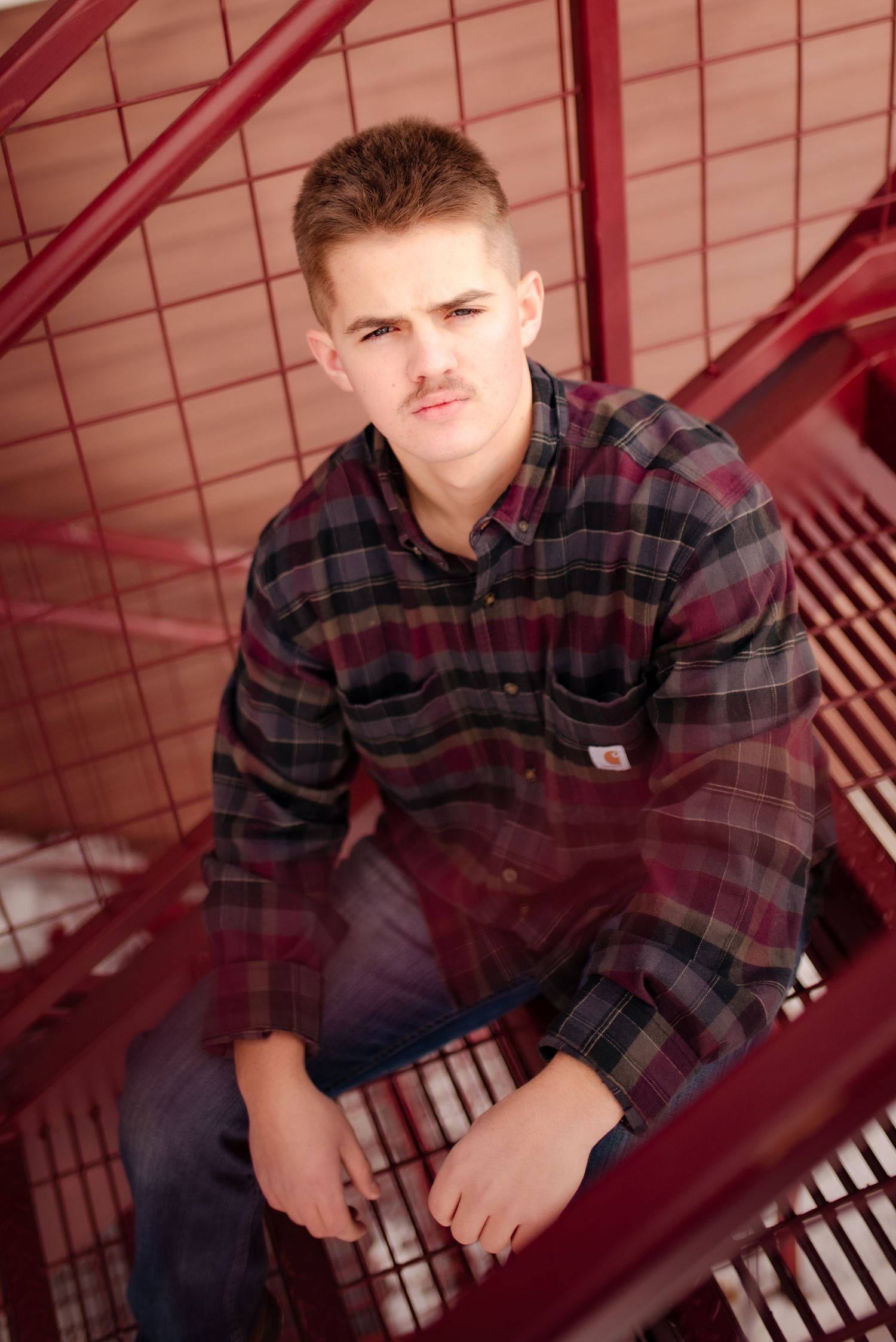 Young person in plaid flannel shirt sitting on red metal stairs in casual pose.