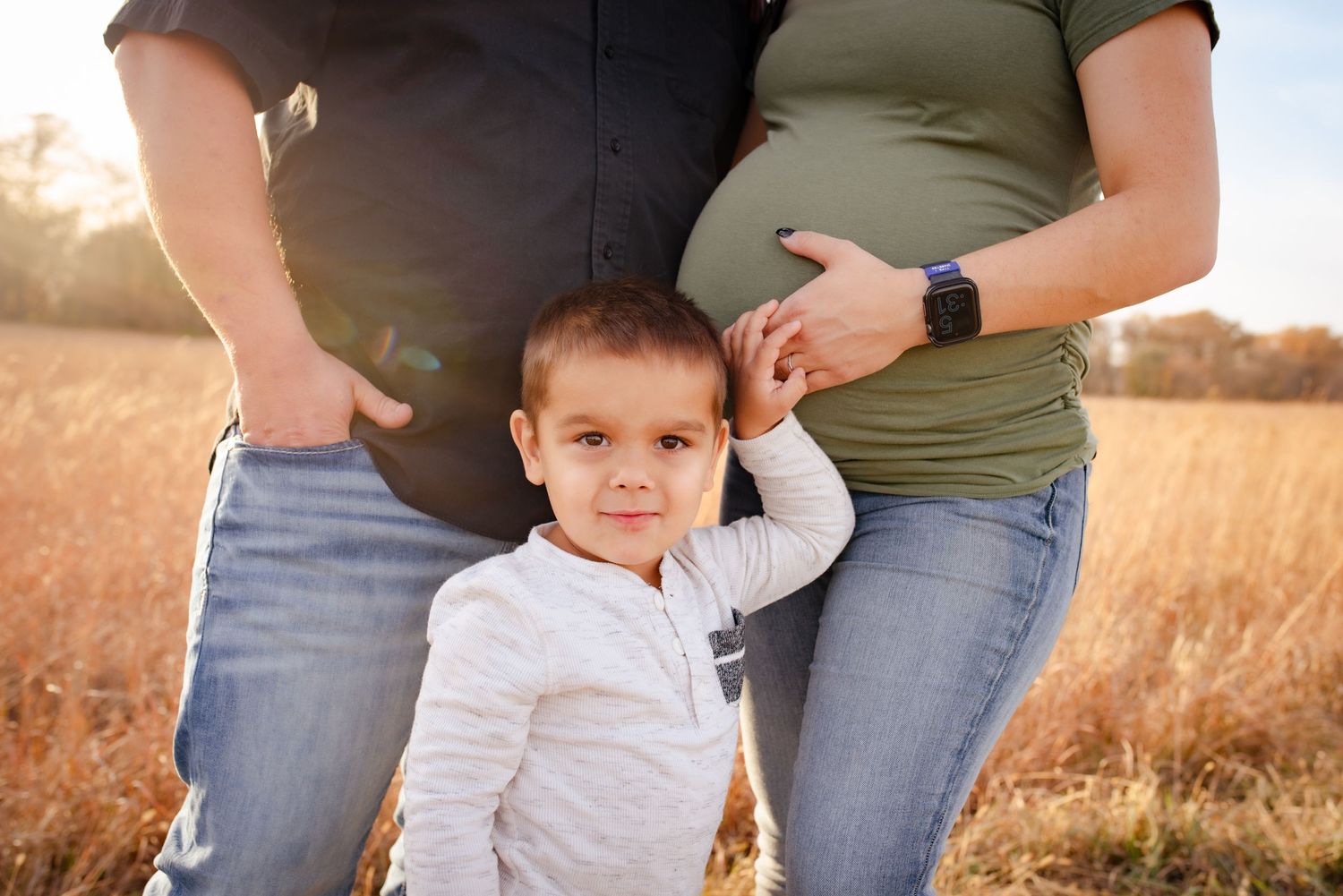 Young child poses between adults in a rustic field setting.