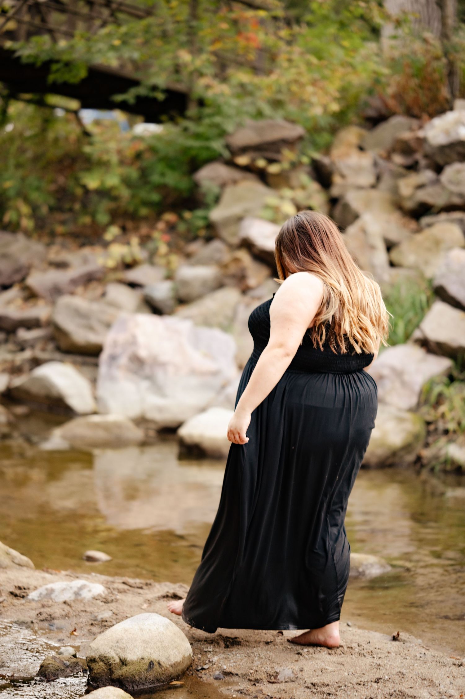 A candid riverside photo showing a black dress against natural stone and water elements.