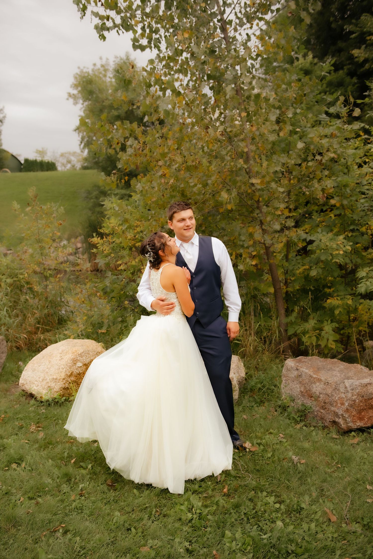 A couple shares a romantic moment on their wedding day surrounded by autumn trees and large rocks.