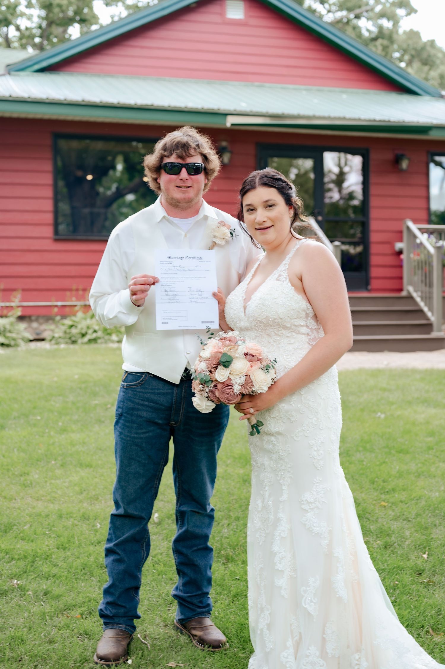 Newlyweds display their marriage certificate in front of pink building with green roof.