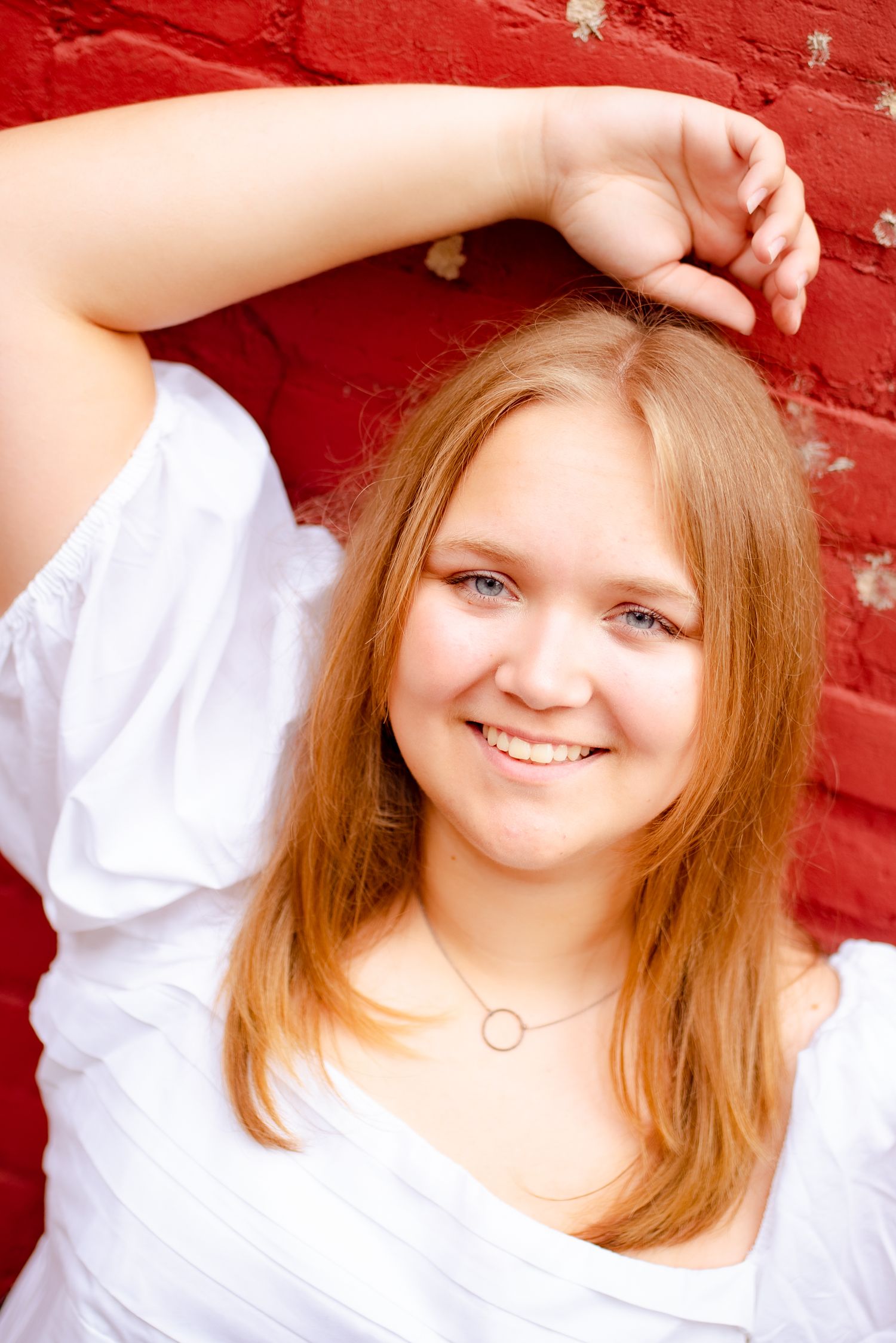 Portrait against red brick wall with person in white top and delicate necklace.