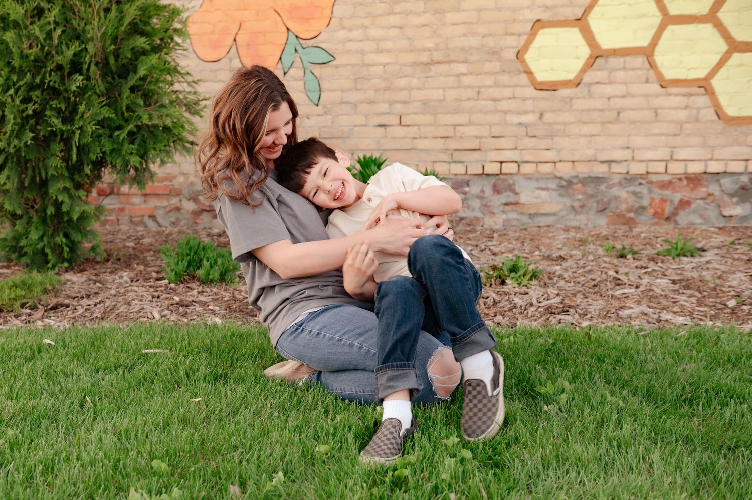 Playful tickling moment captured outdoors against brick wall with painted honeycomb design.