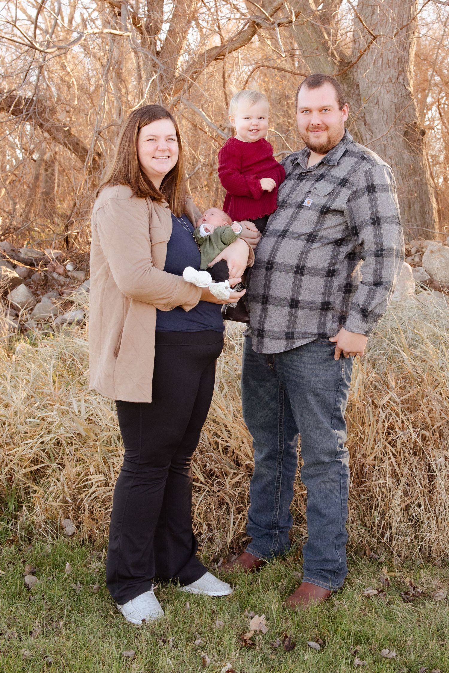 A family of three posed together outdoors against a backdrop of autumn foliage.
