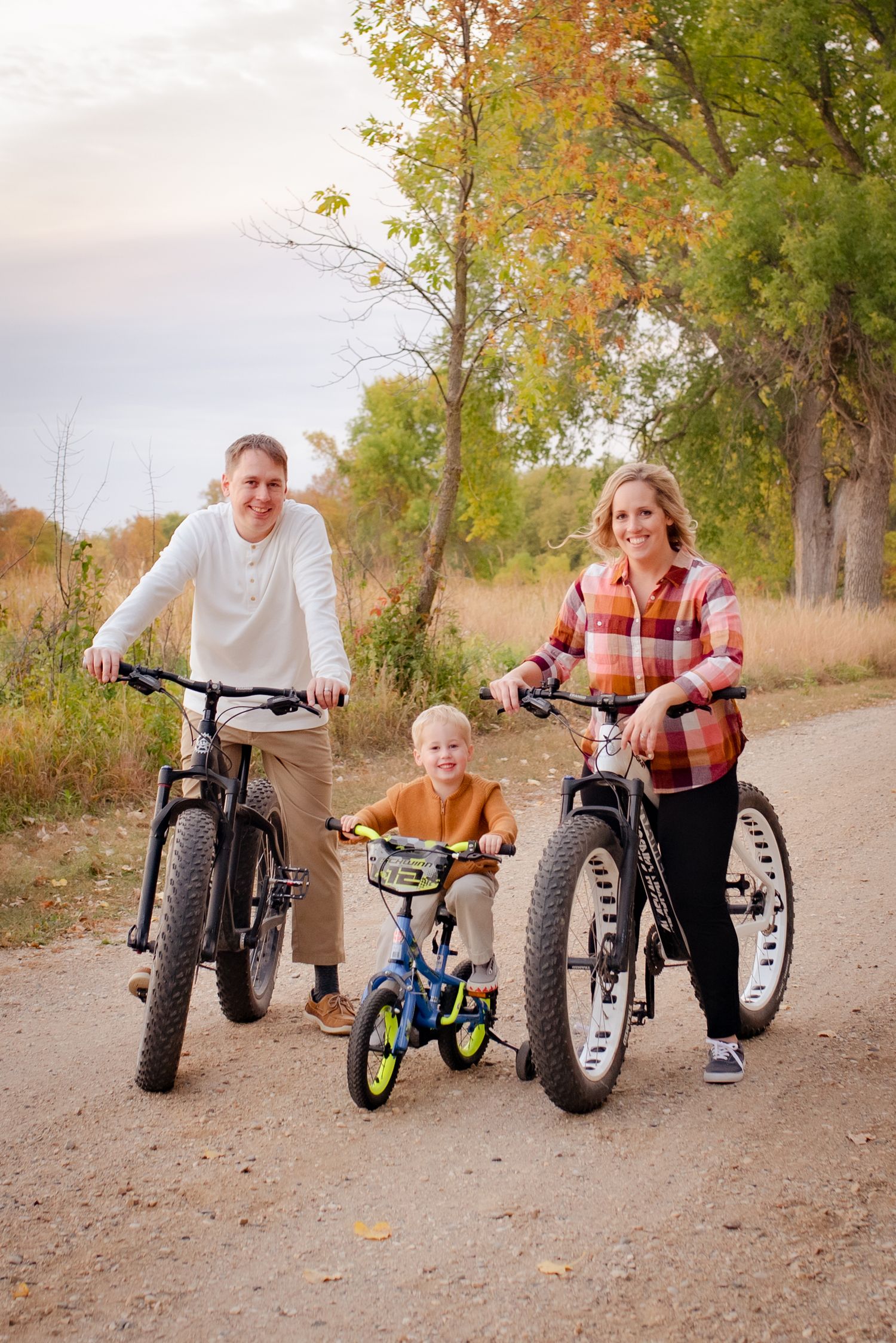 A family poses with their bicycles on a trail during autumn, featuring fat tire bikes and a small blue bike.