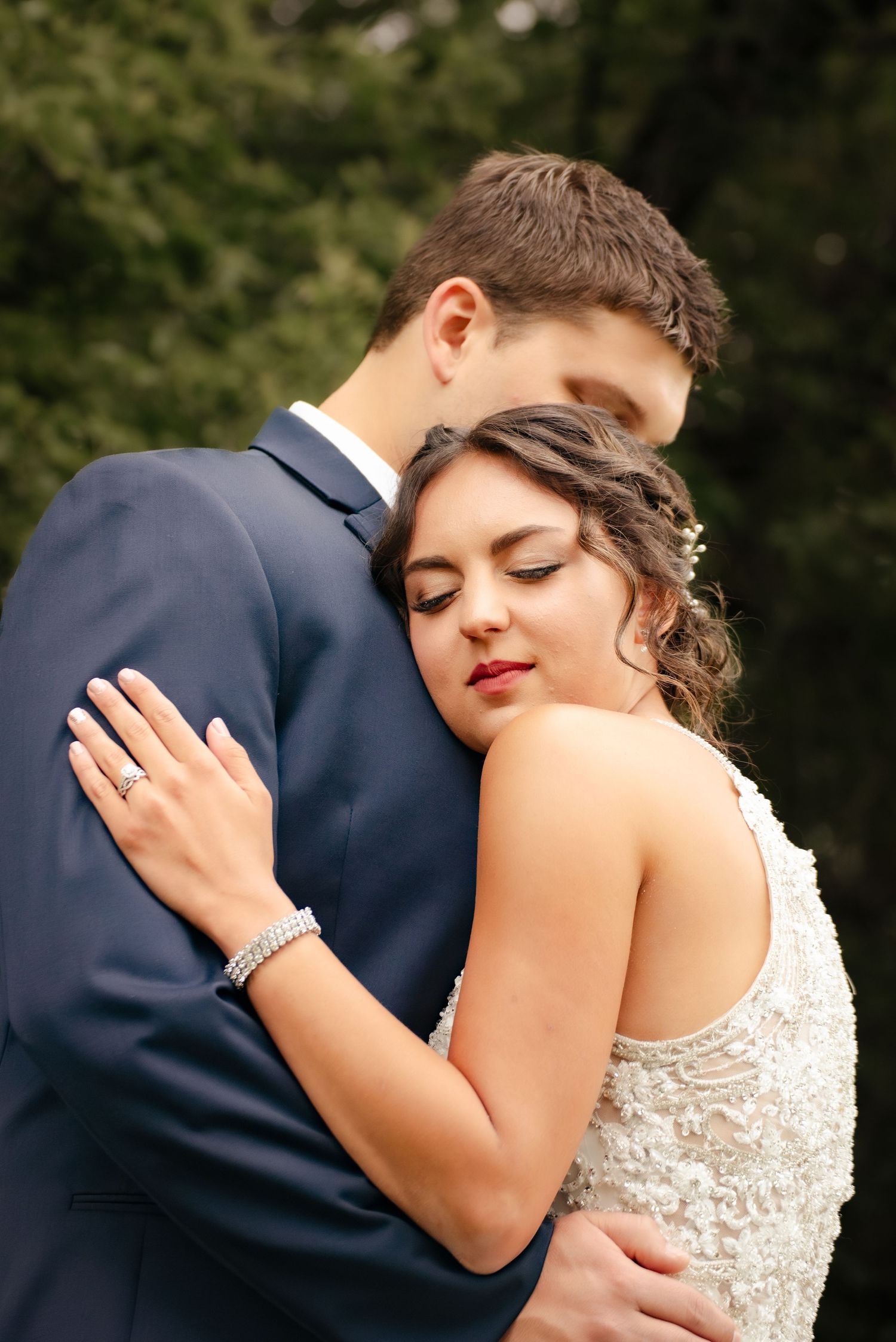 Intimate wedding portrait showing tender embrace between bride in lace gown and groom in navy suit.