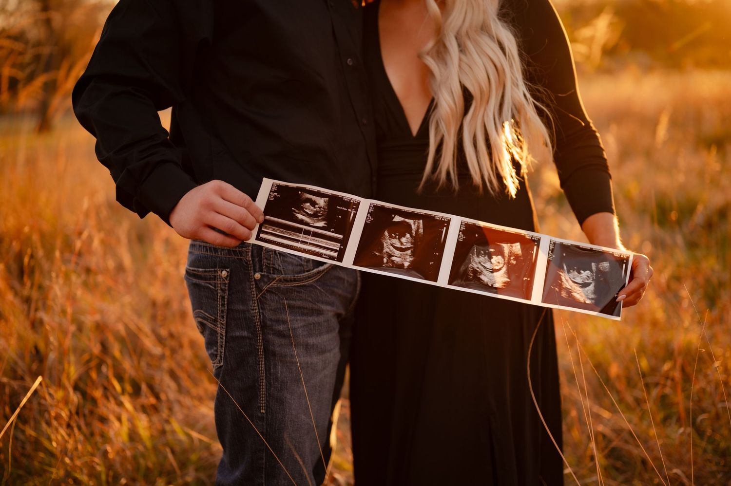 Couple holding ultrasound photos during fall outdoor pregnancy announcement photoshoot.