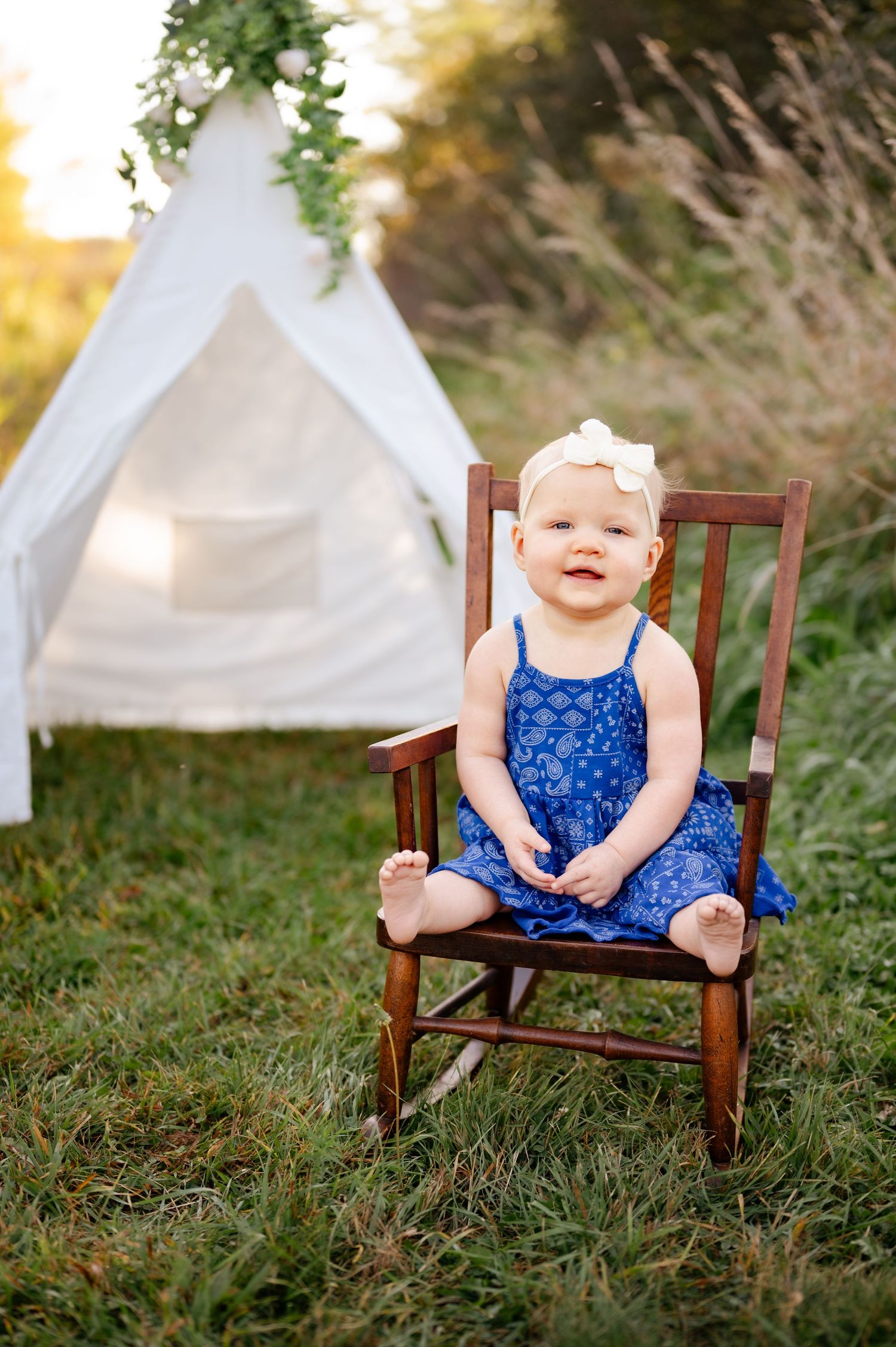 White tent and wooden rocking chair set up for outdoor photo session in a grassy field.