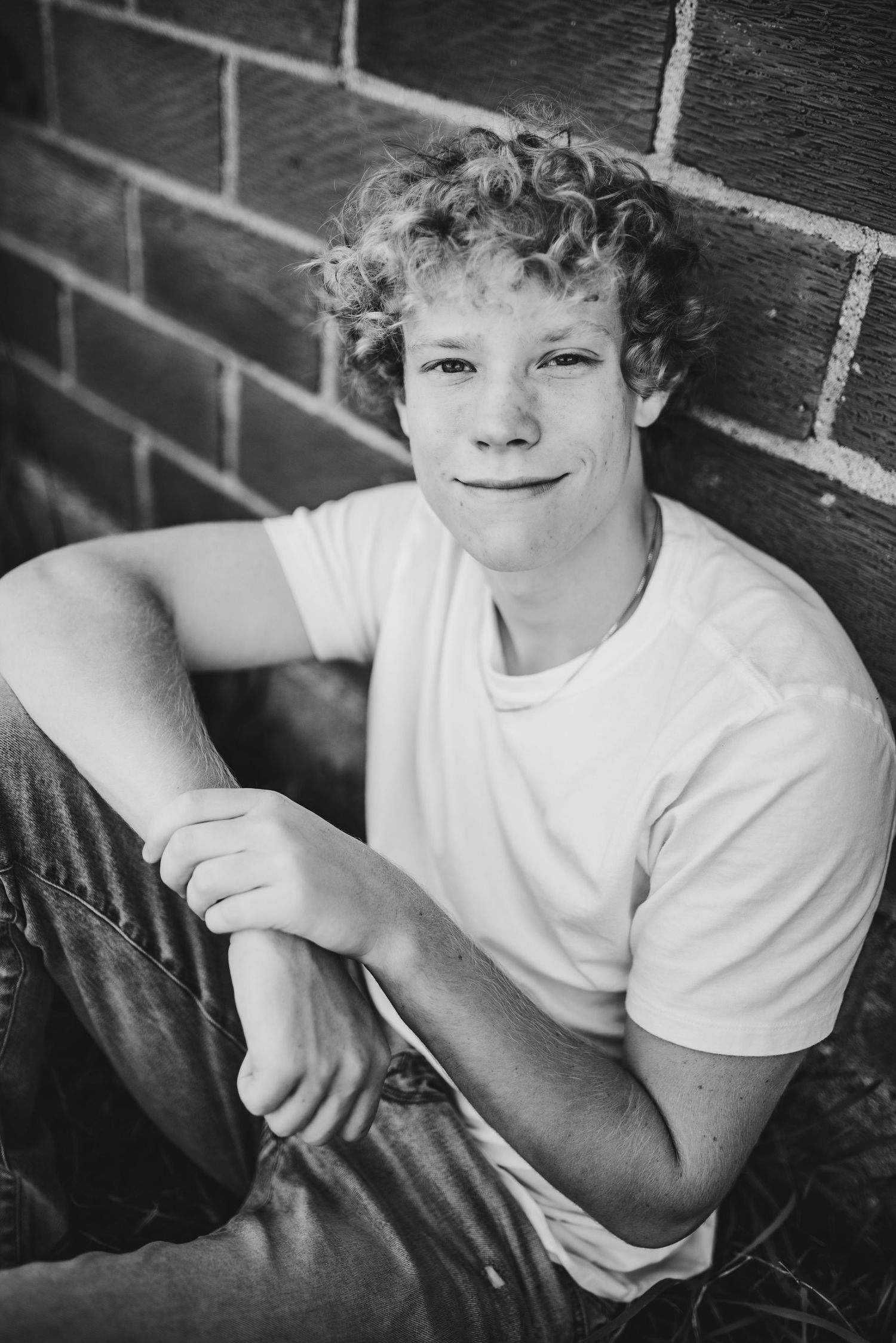 Black and white portrait against brick wall featuring casual white t-shirt and natural lighting.