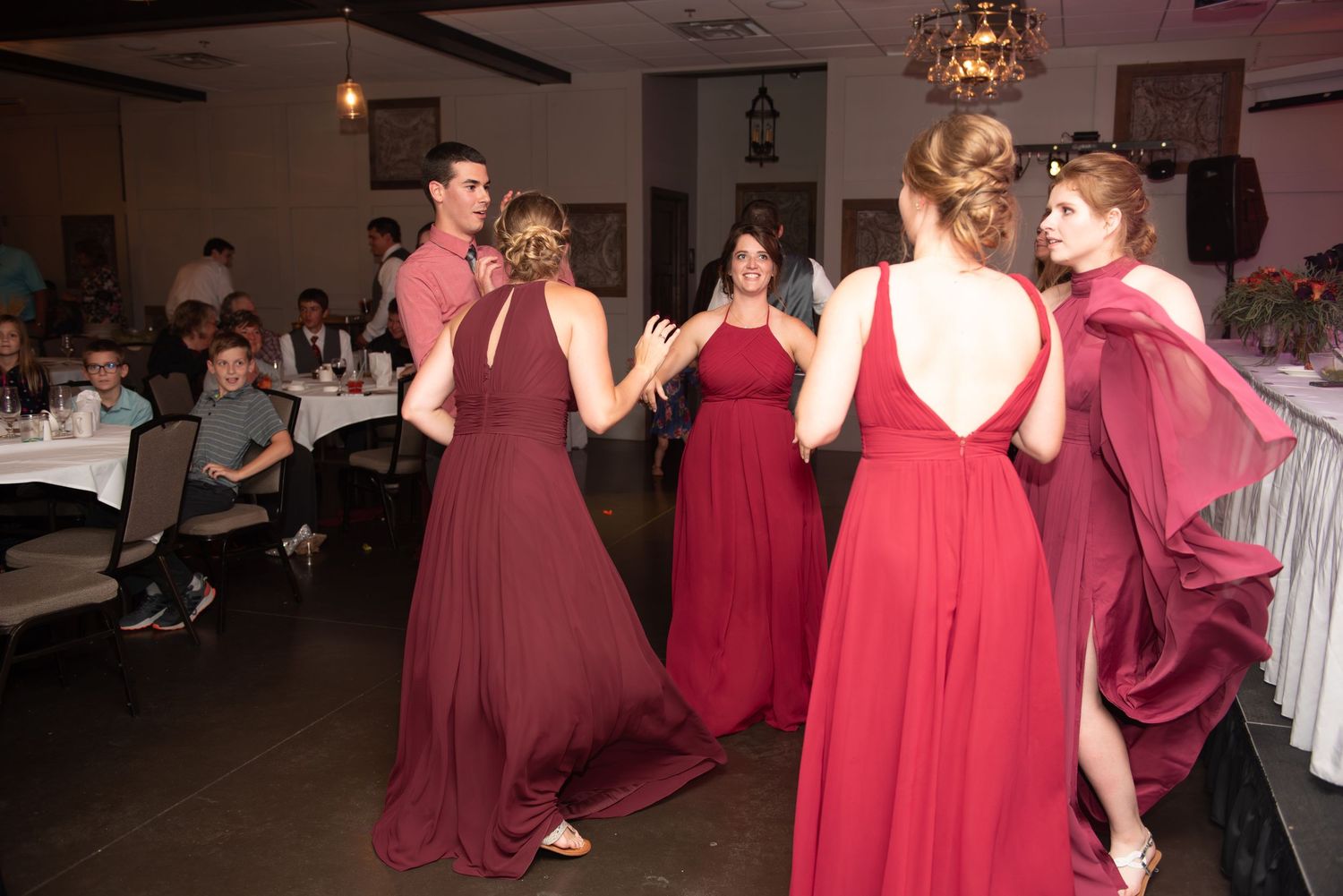 Wedding party in burgundy dresses dancing and celebrating on dance floor.