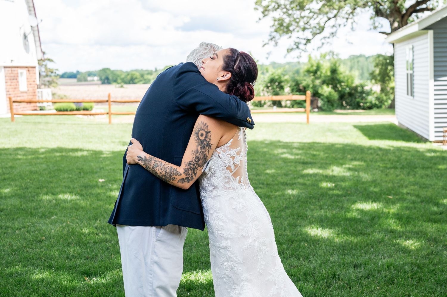 Tender embrace on grassy lawn during outdoor wedding celebration.