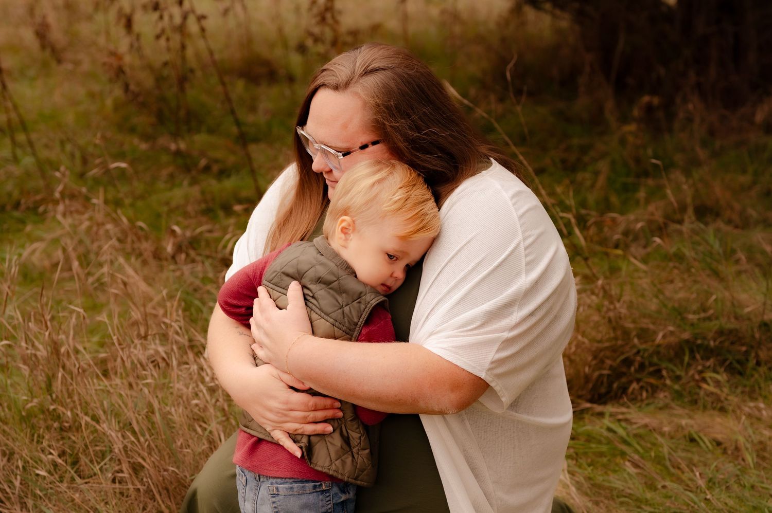 A couple embraces tenderly in a romantic outdoor setting with natural lighting and greenery in the background.