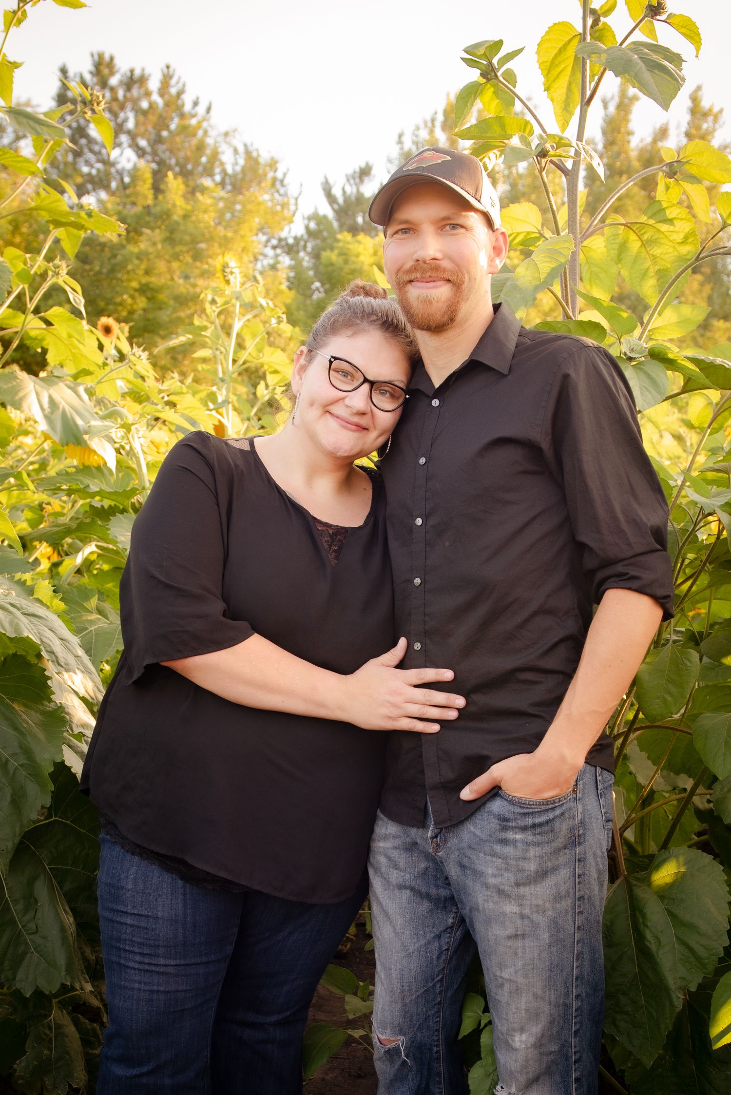 Couple sharing an intimate moment in front of sunlit garden foliage.