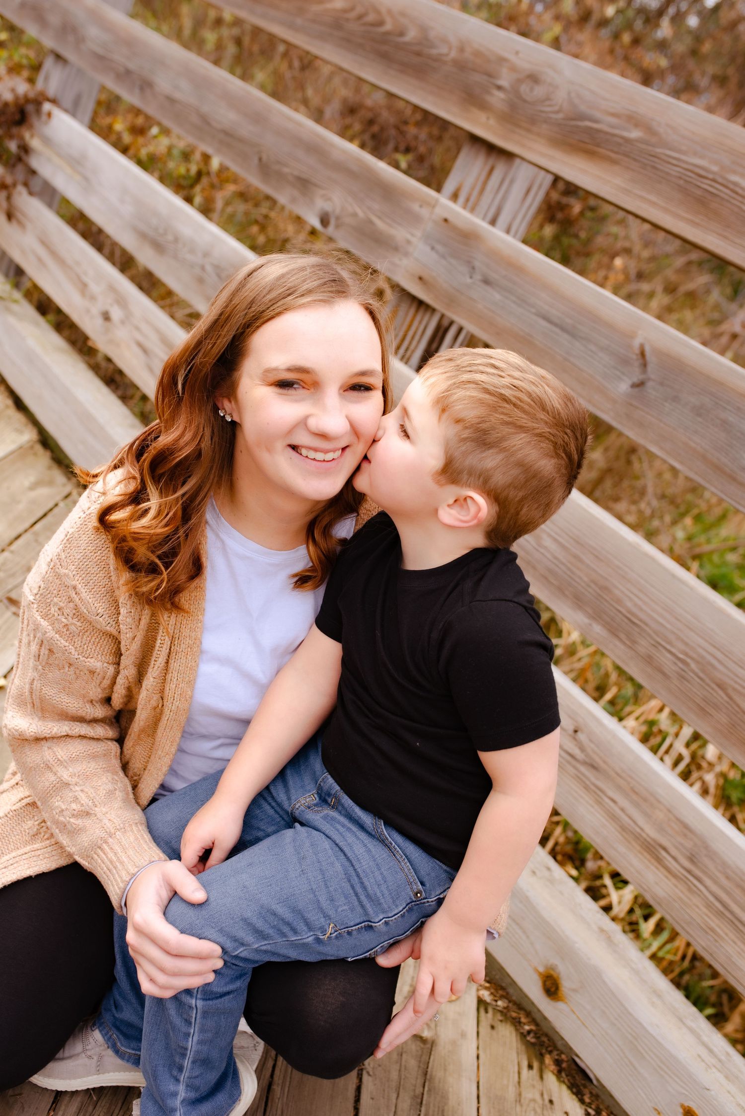 A heartwarming embrace shared between two people on a wooden bench surrounded by fall foliage.