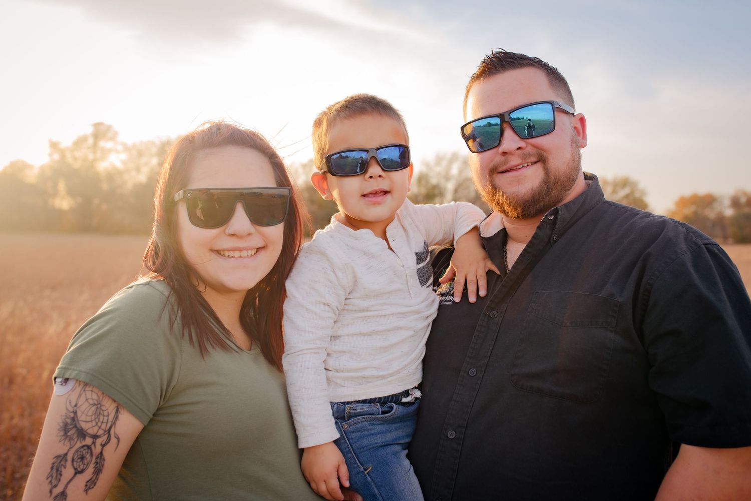 Family wearing sunglasses poses together in sunny field during outdoor photoshoot.