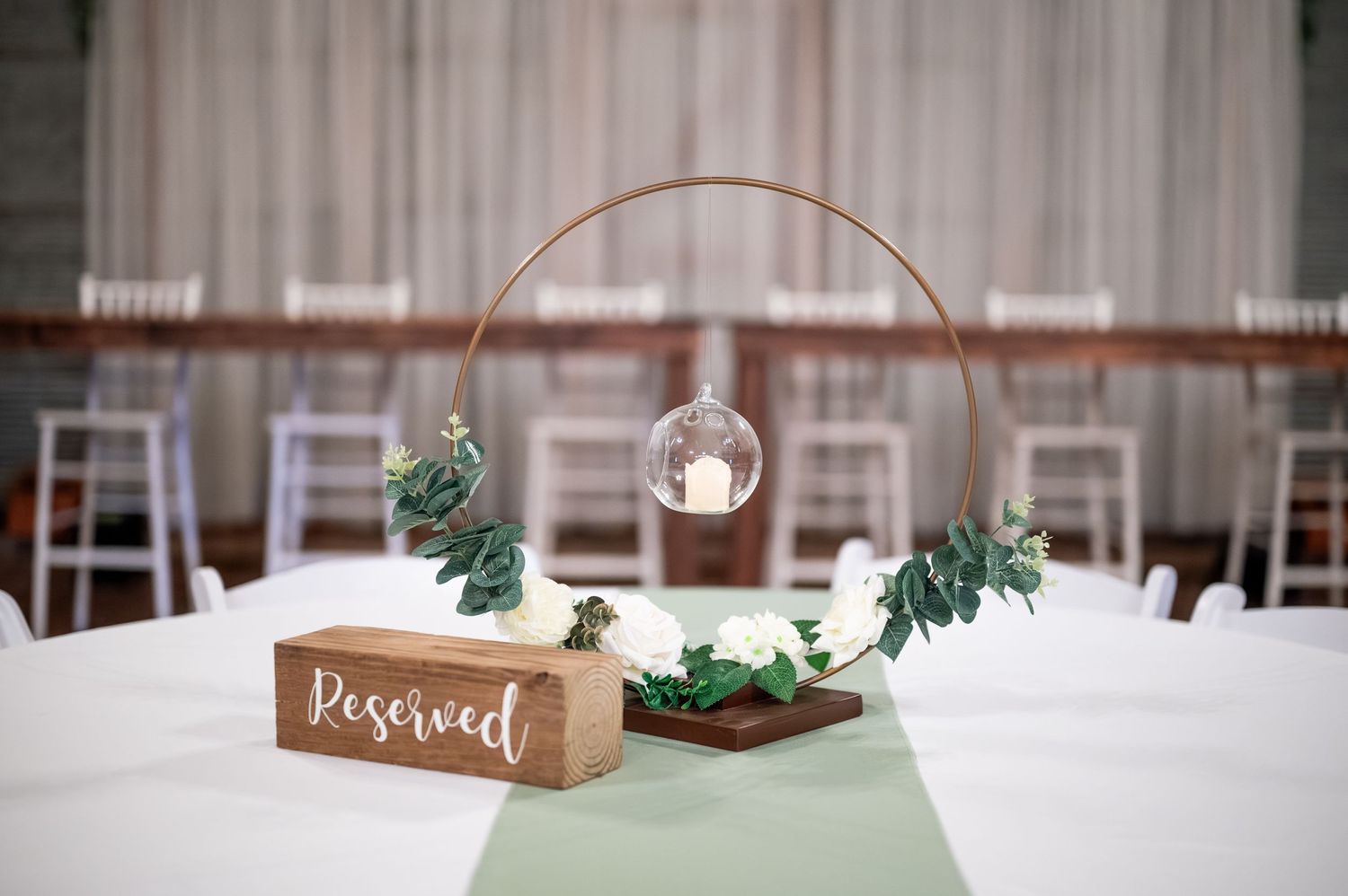 Minimalist wedding table centerpiece with geometric arch, greenery and reserved sign on white tablecloth.