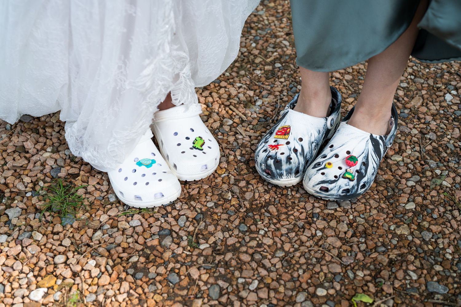 Two pairs of decorated Crocs shoes shown on gravel at a wedding.