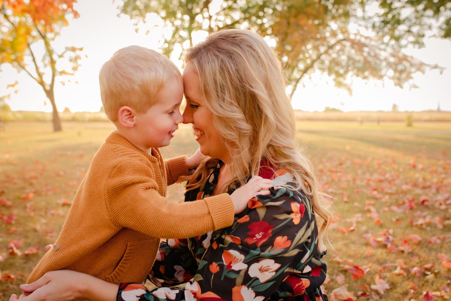 Tender autumn moment in fallen leaves with floral dress and orange sweater.